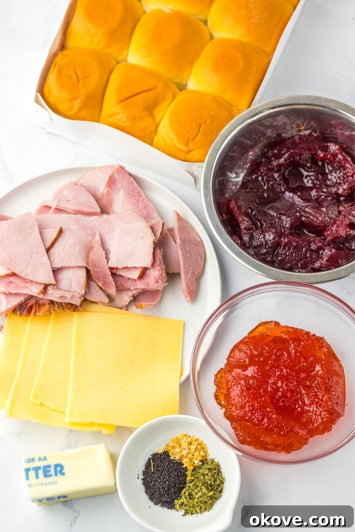 Festive Finger Sandwiches 3 Ingredients needed to make ham and cranberry holiday sliders measured in bowls on a marble table.