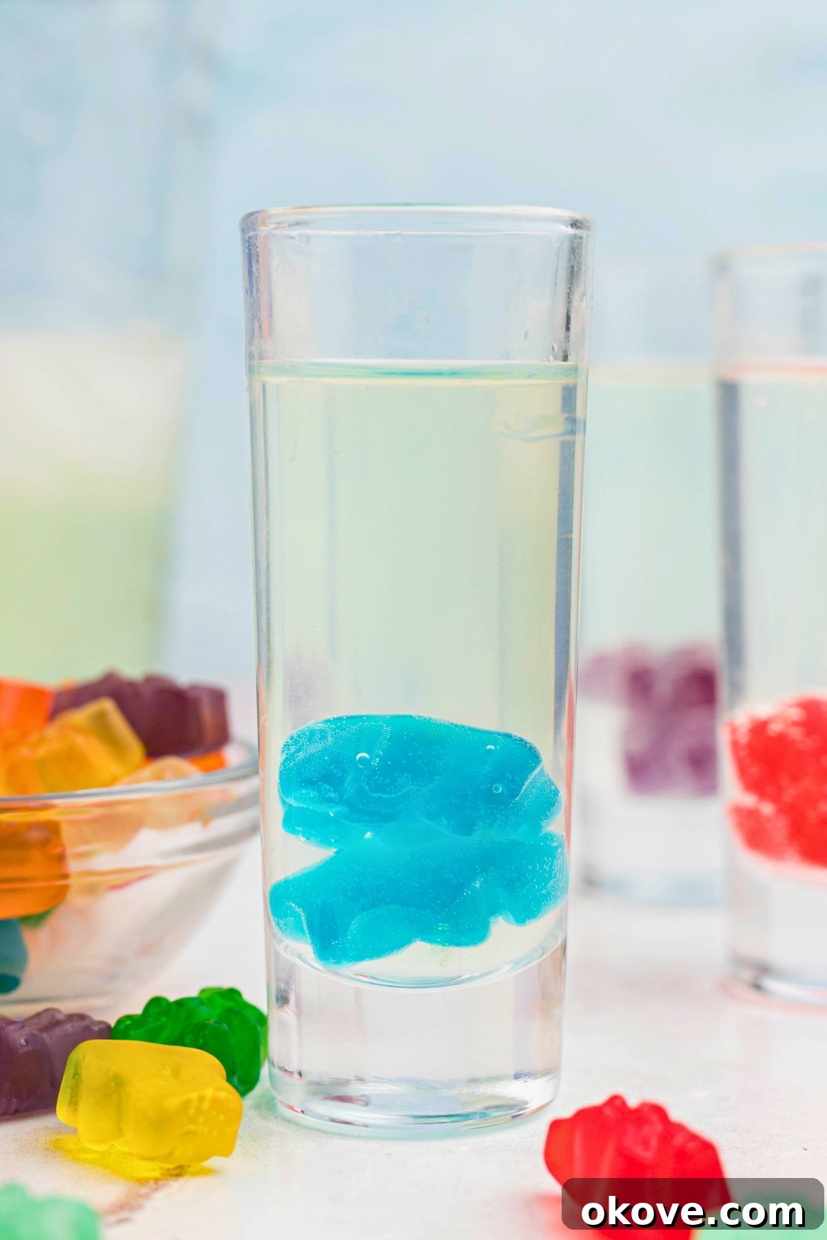 Beary Boozy Bliss 6 Shot glass filled with vodka and other liquids, with gummy bears dropped inside of the glass and on the table.