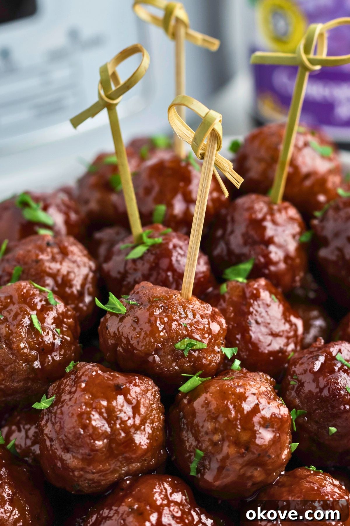 Grape jelly meatballs stacked with some skewered, in front of a slow cooker and jar of grape jelly. A perfect sweet and savory party appetizer.