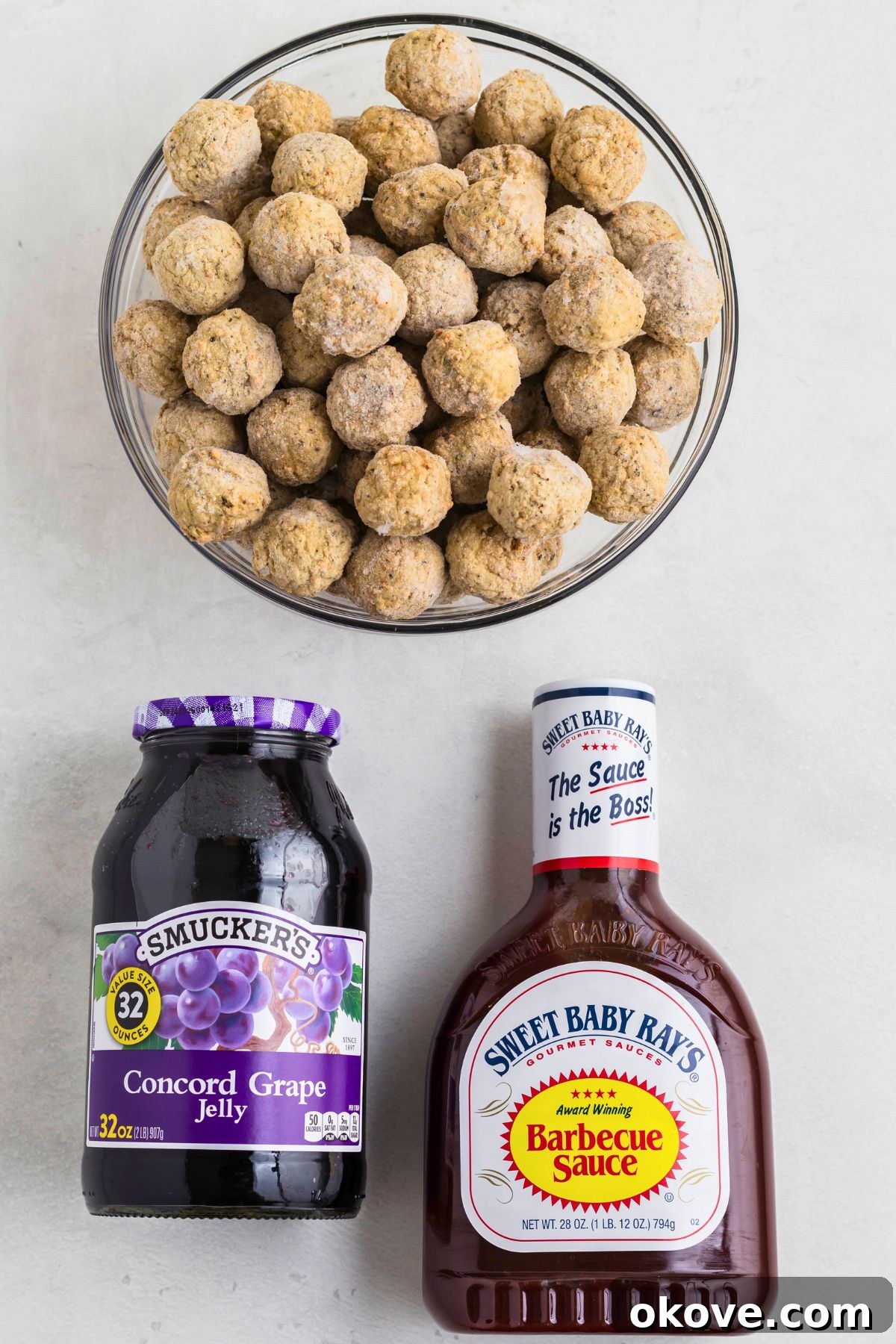 Frozen meatballs, grape jelly, and BBQ sauce, on a white marble table before mixing together in a crock pot and cooking. Key ingredients for an easy slow cooker recipe.