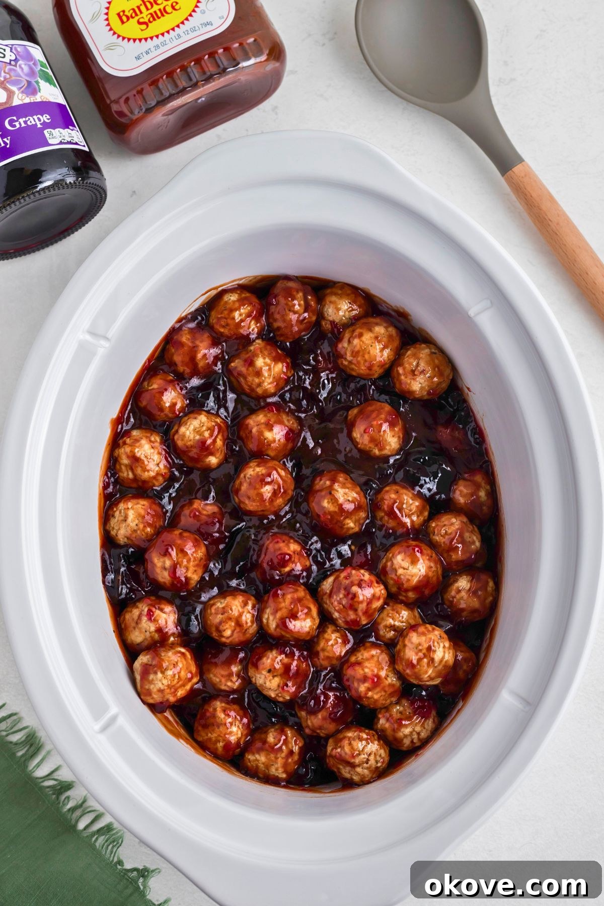 Grape jelly meatballs being cooked in a crock pot. The sauce is bubbling and coating the meatballs.