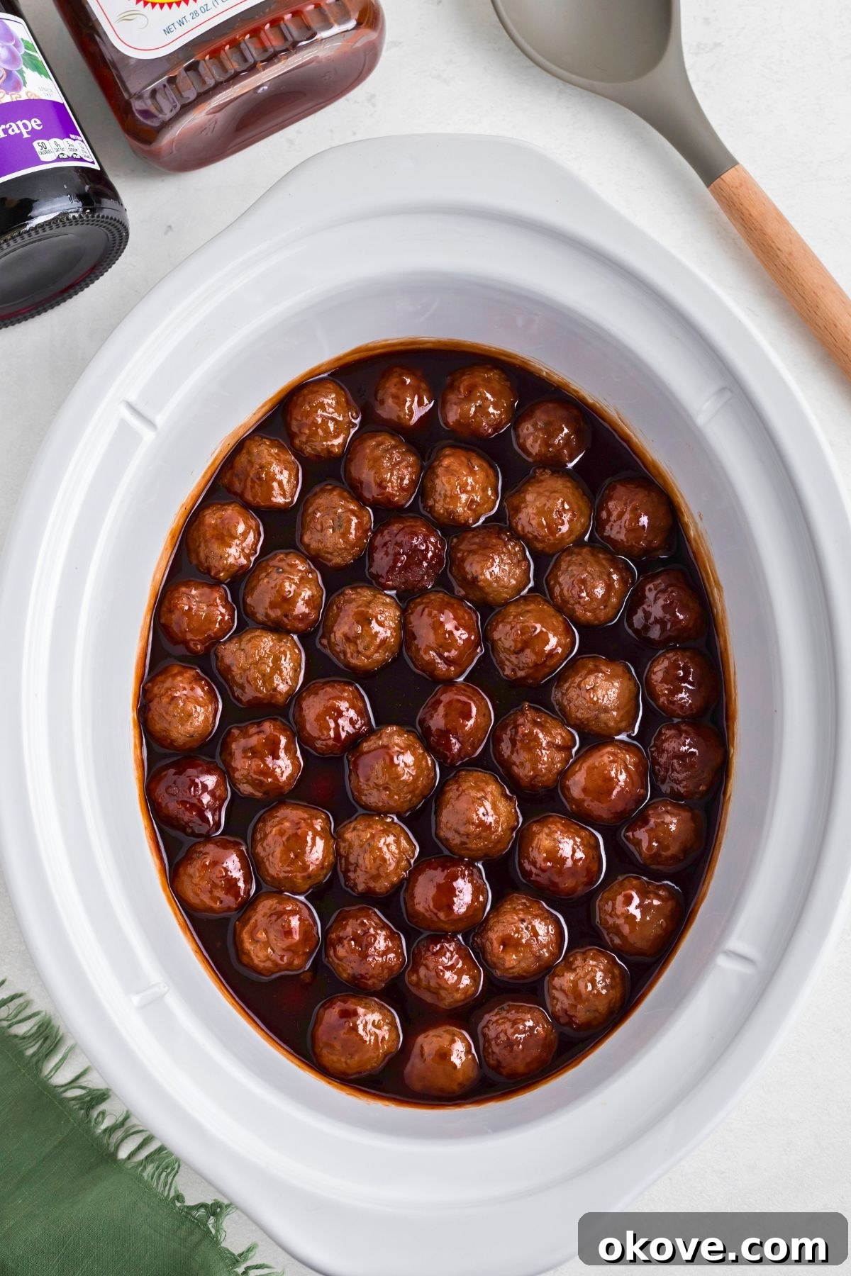 Grape jelly meatballs in a white slow cooker after cooking for 3-4 hours. The sauce has thickened.