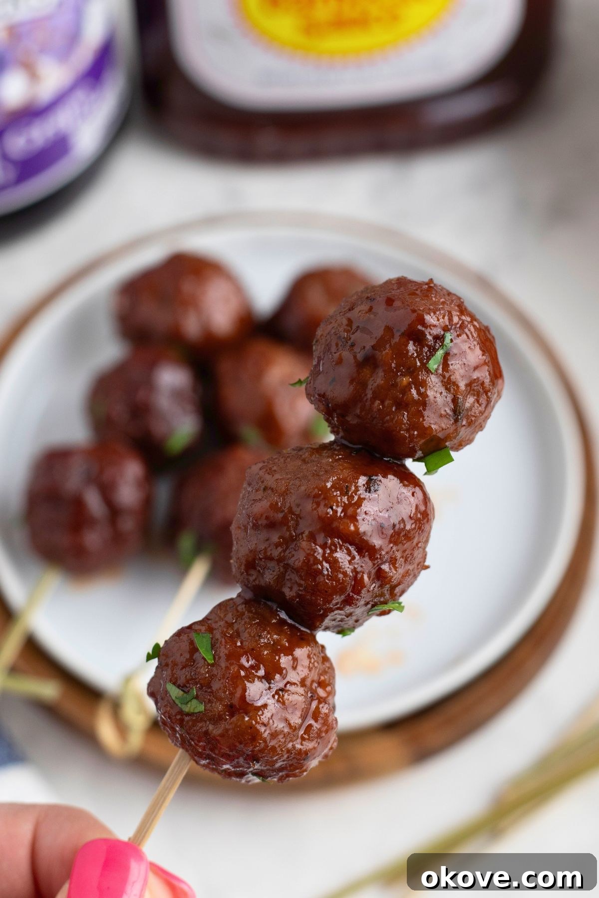Three meatballs on a skewer over a small white appetizer plate. A perfect serving suggestion for party food.