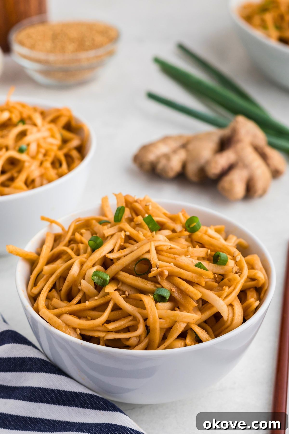 Blazing Noodle Bliss 2 Juicy spicy noodles in a white bowl, garnished with green onions next to a blue and white striped linen.