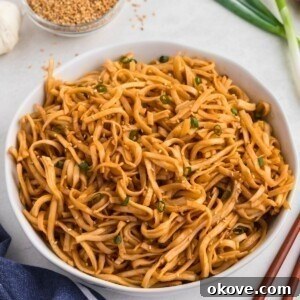 Spicy noodles tossed with sauce, served in a white bowl with chopsticks next to the bowl.