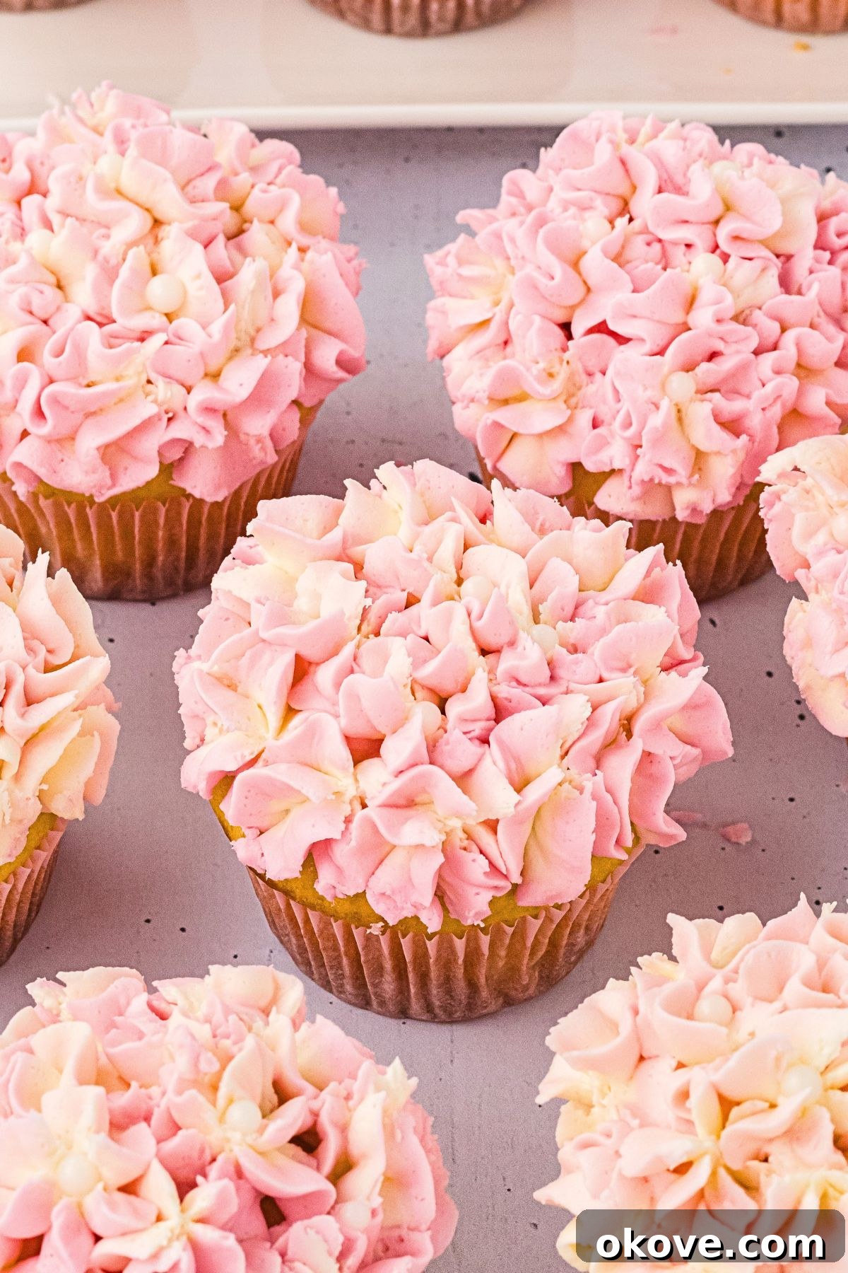 Frosted pink hydrangea cupcakes on a white table. 
