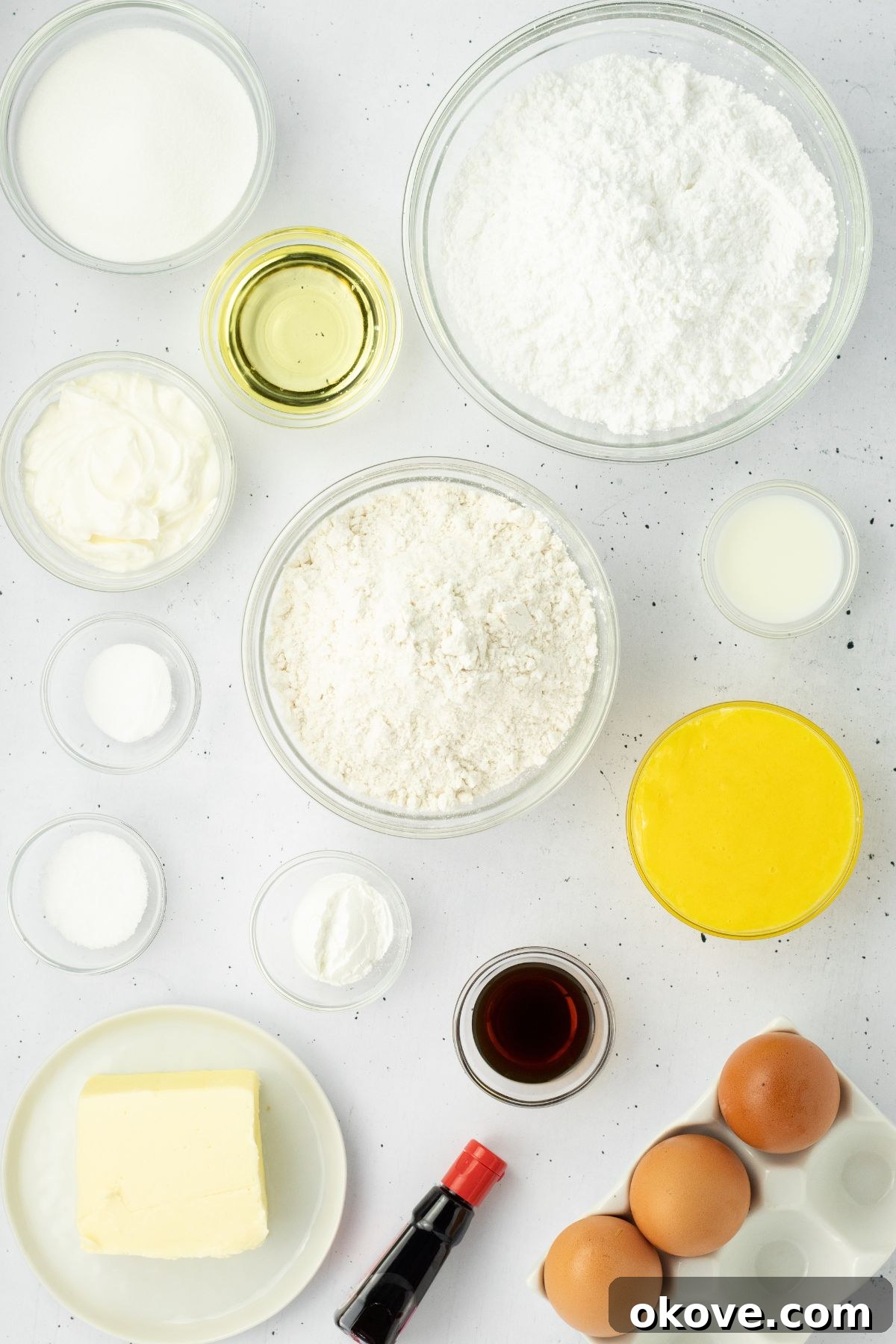 Ingredients needed to make vanilla cupcakes measured into small glass bowls and laid out on a white marble table. 