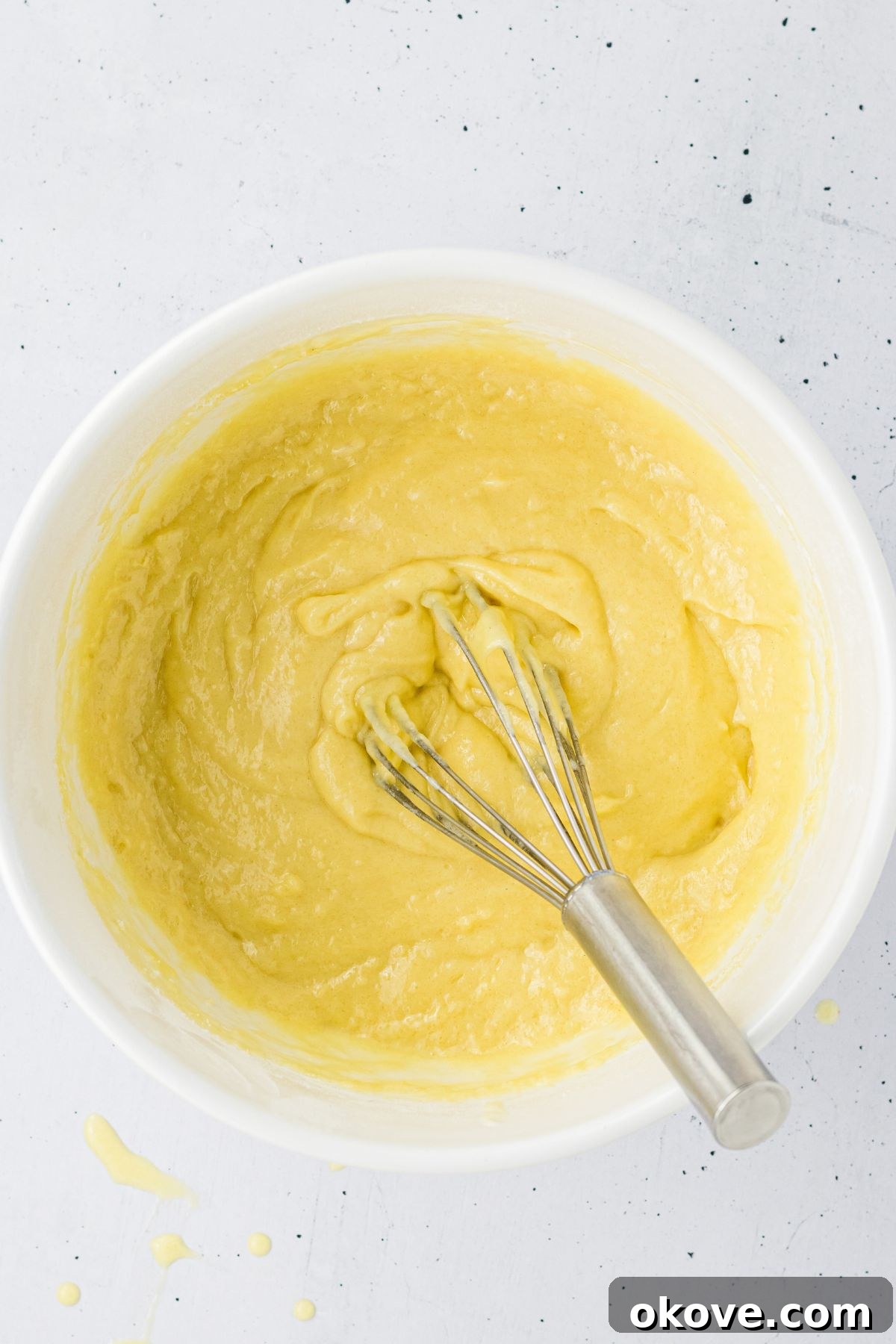 Cake batter being whisked together in a white mixing bowl. 