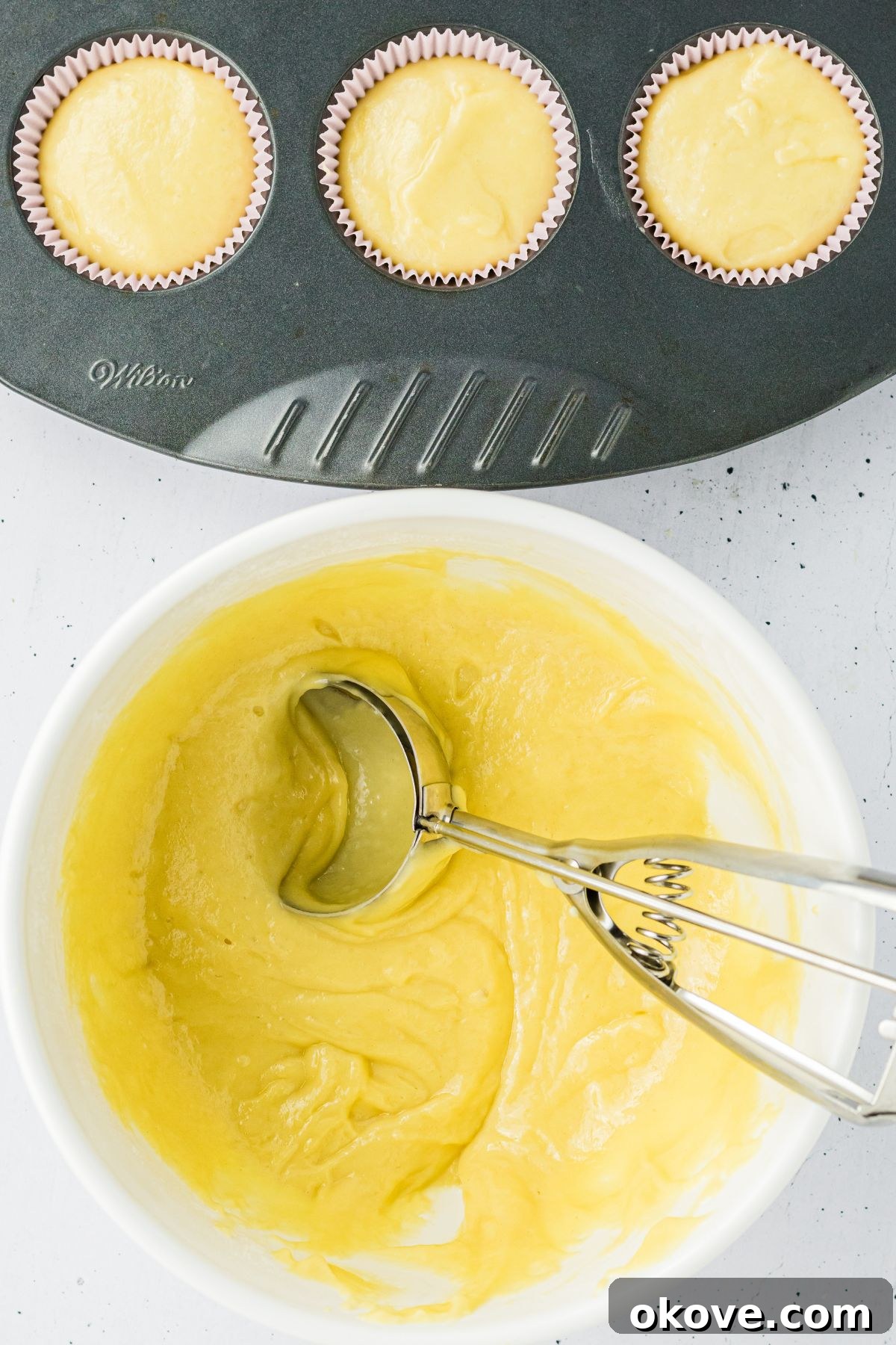 Cake batter being scooped into paper liners to make cupcakes. 
