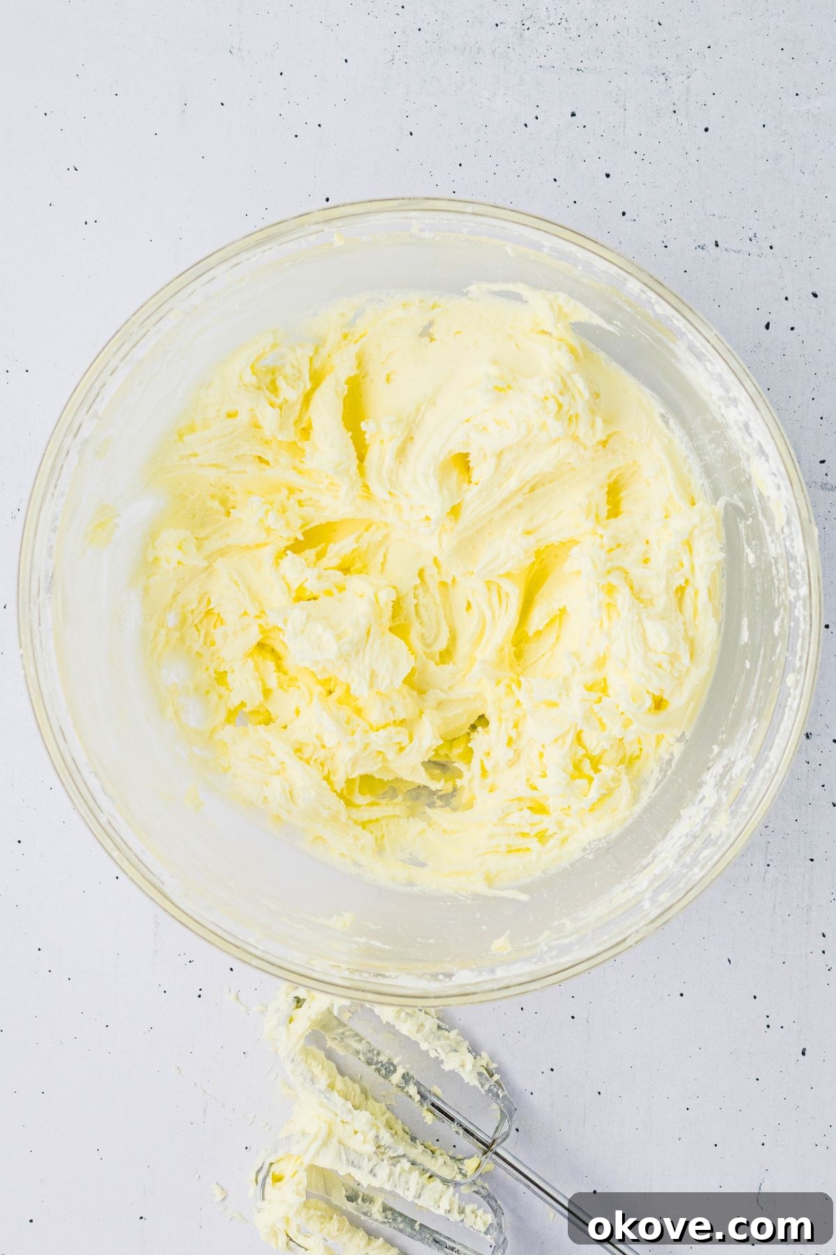 Buttercream frosting being mixed in a clear glass mixing bowl. 