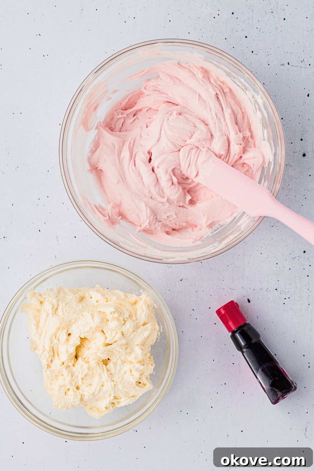 Buttercream frosting divided into two bowls, with one bowl having pink coloring added making pink frosting. 