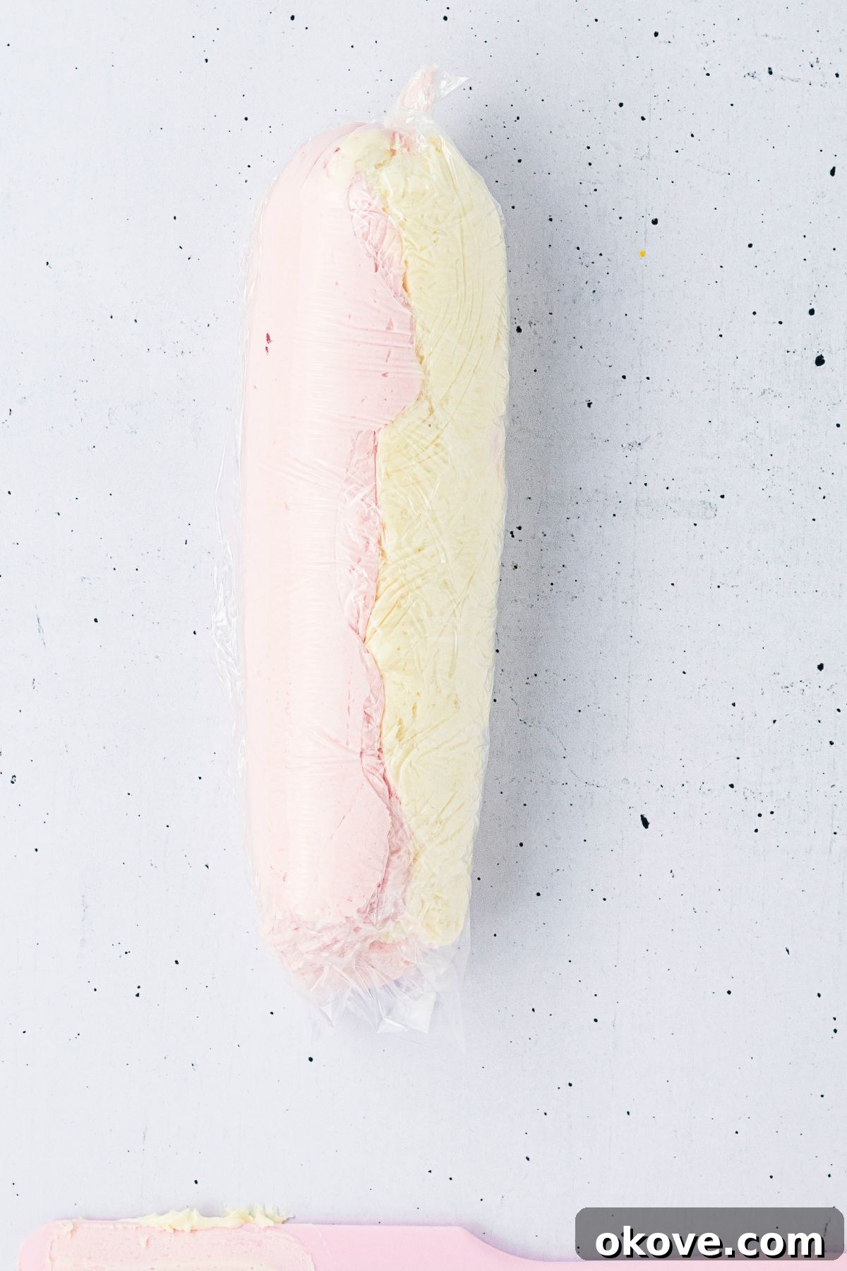 Pink and white frosting shown side by side and then wrapped in plastic wrap. 