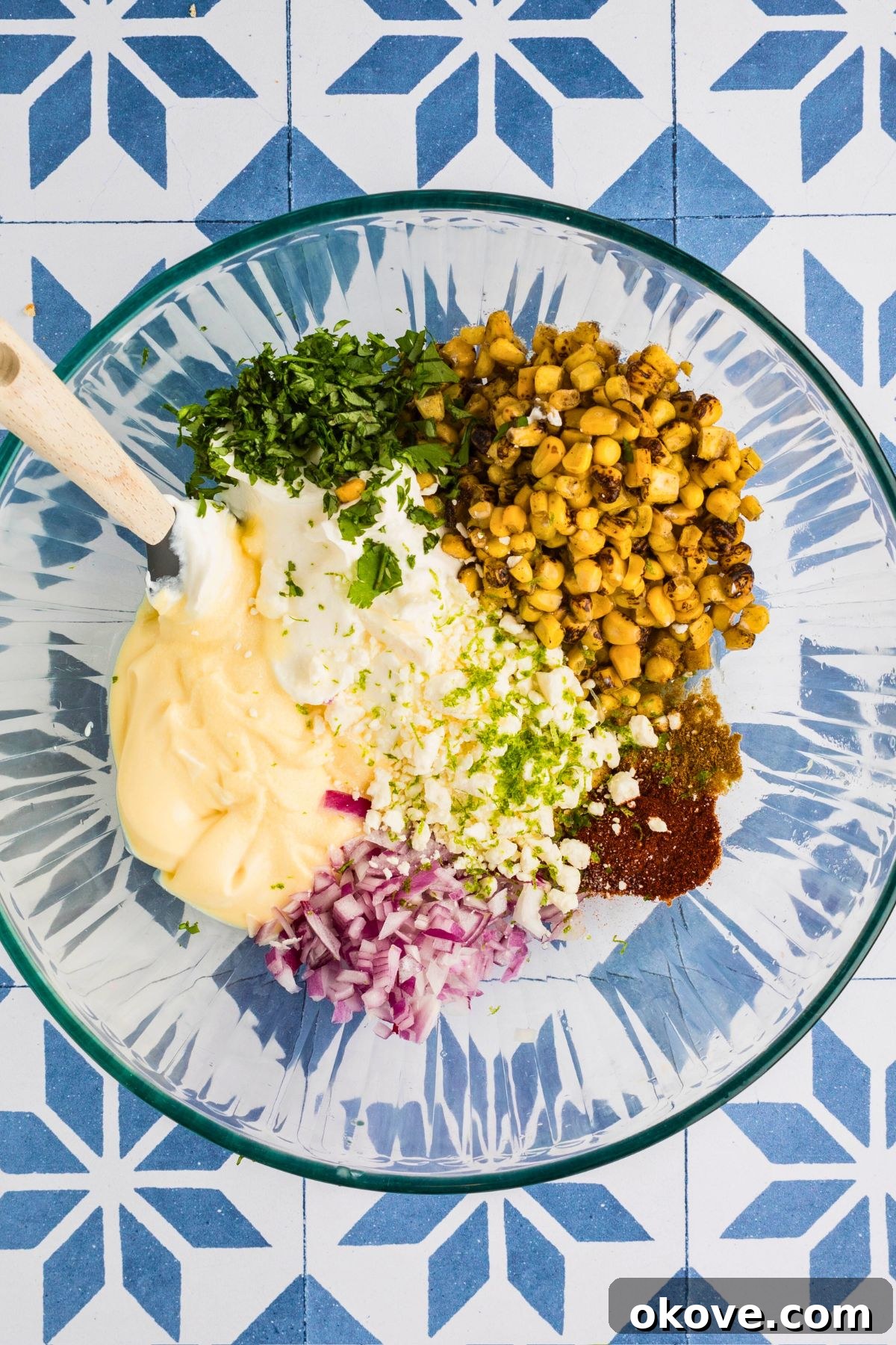 Fiesta Elote Dip 4 Spices, cheese, fire-roasted corn, and creamy ingredients beginning to mix together in a clear glass mixing bowl for the corn dip, illustrating the initial mixing process.