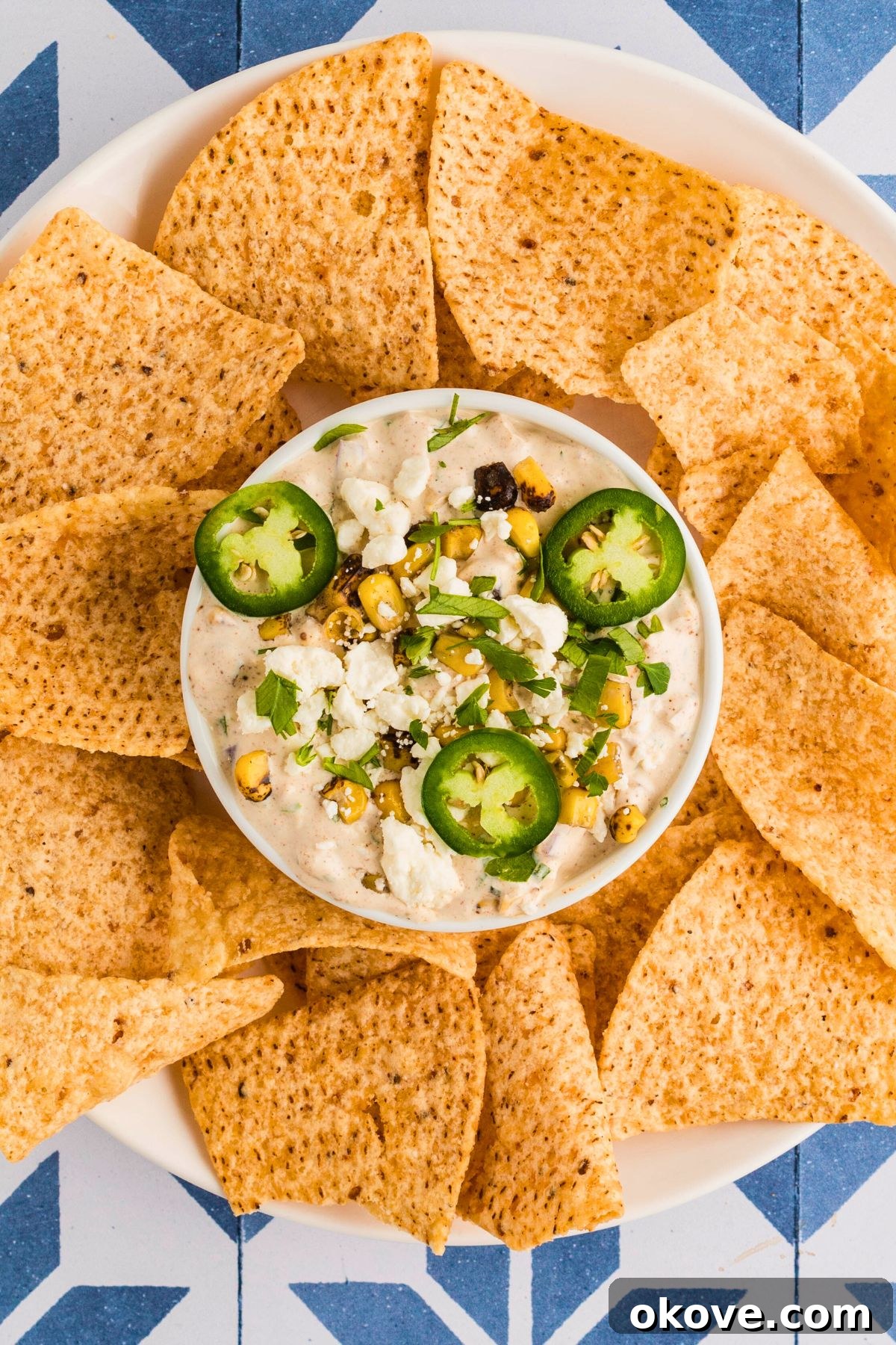 Fiesta Elote Dip 6 A small bowl of creamy Mexican street corn dip, garnished with fresh cilantro and a sprinkle of cotija cheese, surrounded by crispy tortilla chips, ready for dipping.