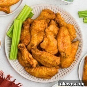 Crispy baked chicken wings, tossed in buffalo sauce, on a white plate with celery sticks.