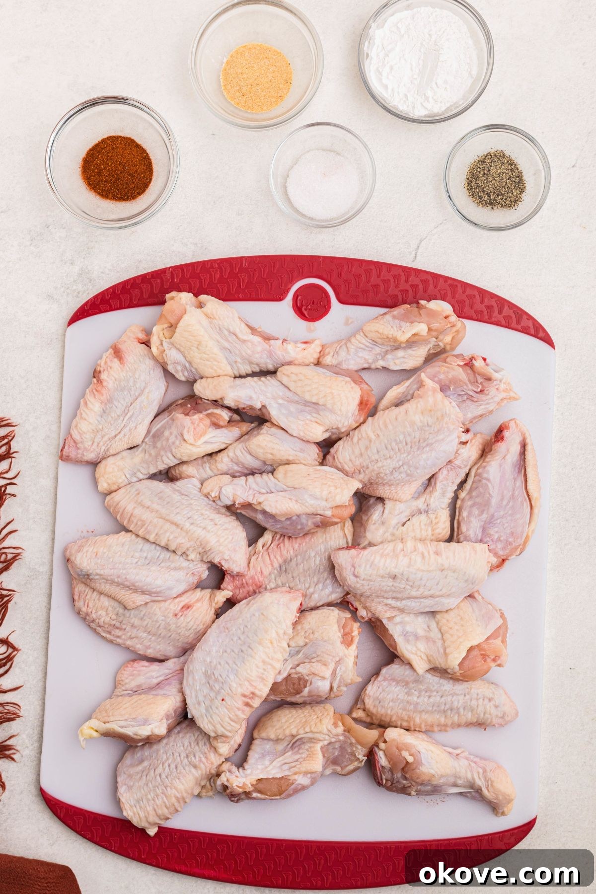 Golden Crispy Wings 3 Uncooked chicken wings on a cutting board, surrounded by small glass bowls with baking powder, garlic powder, smoked paprika, salt, and black pepper.
