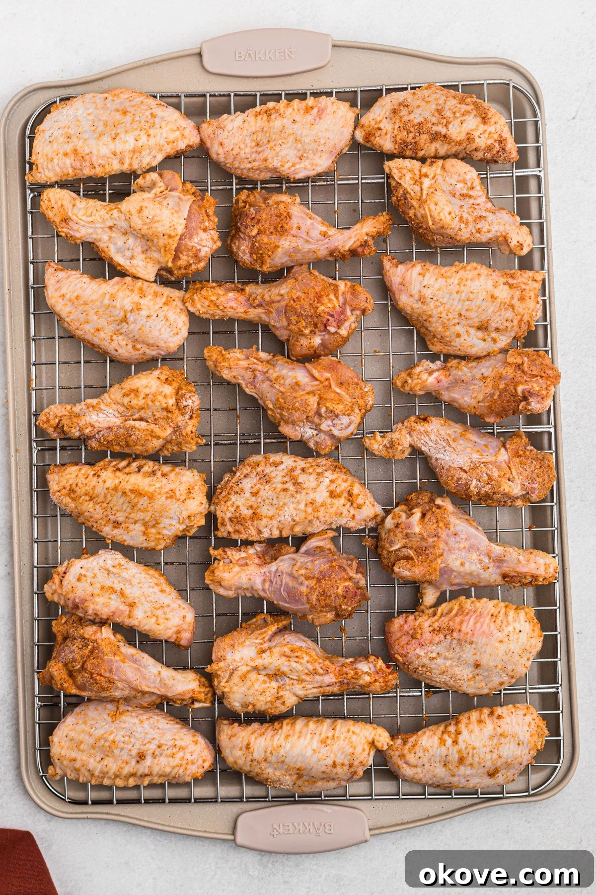 Golden Crispy Wings 5 A baking sheet with a wire rack holding a single layer of uncooked, seasoned chicken wings, spaced evenly apart before baking.