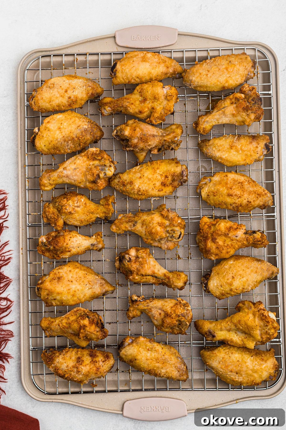 Golden Crispy Wings 6 A close-up of golden and crispy baked chicken wings resting on a wire rack over a baking sheet, freshly removed from the oven and ready to be sauced.
