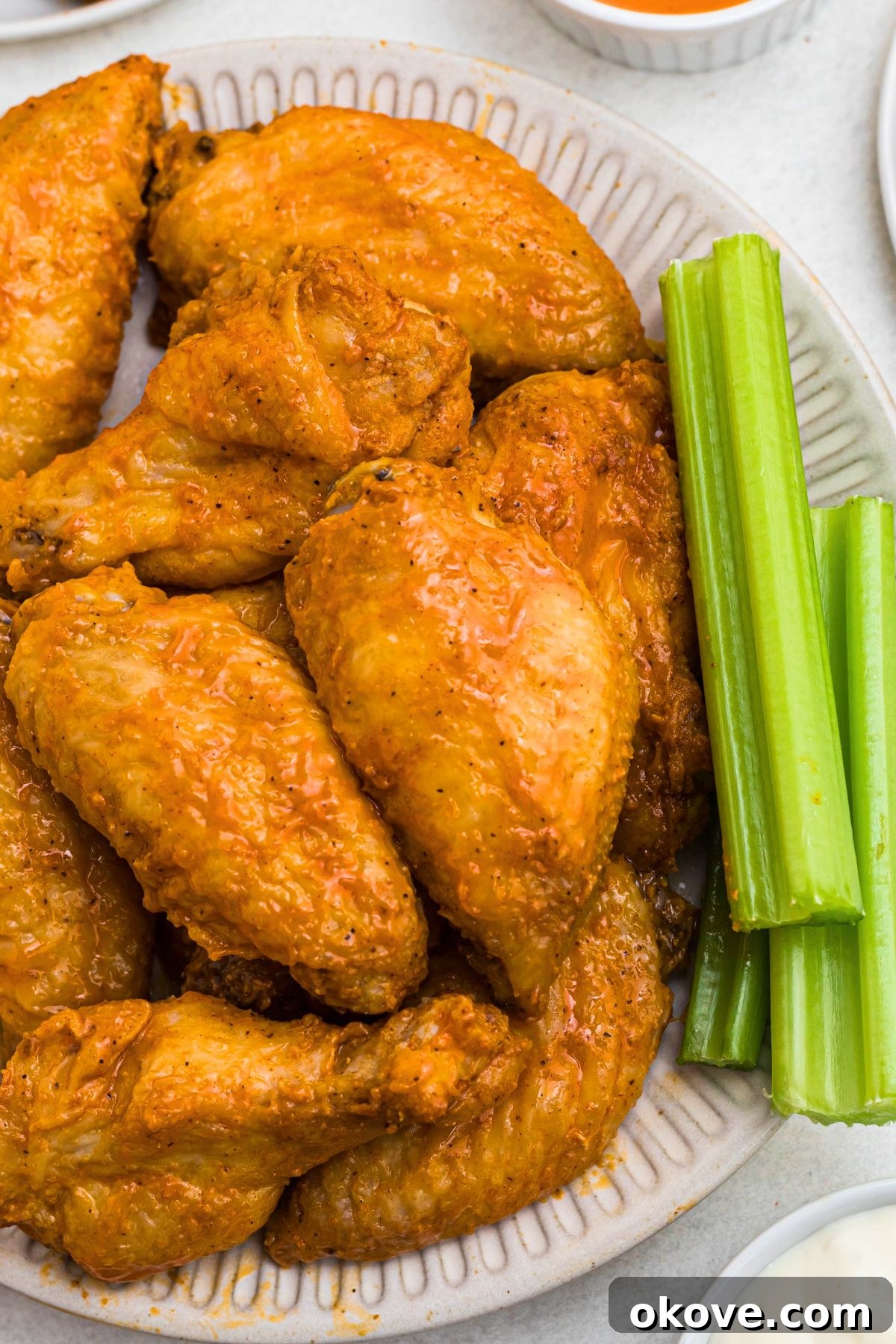 Golden Crispy Wings 8 Three buffalo chicken wings artfully arranged on a white plate with fresh celery sticks for garnish.
