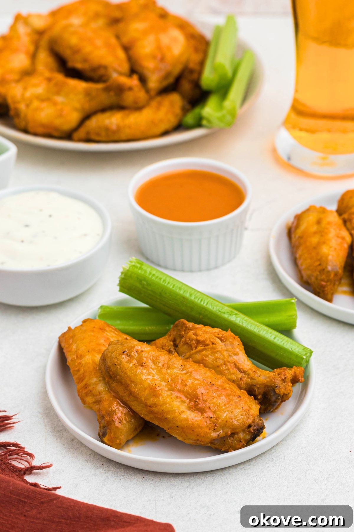 Golden Crispy Wings 9 Three perfectly sauced buffalo chicken wings presented on a white plate, accompanied by crisp celery sticks.