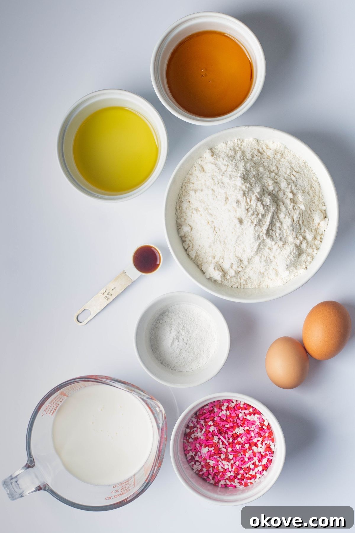 Sweetheart Pancakes 3 All the essential ingredients for making fluffy Valentine's Day pancakes, neatly arranged and measured in small white bowls on a clean white marble tabletop, ready for mixing.