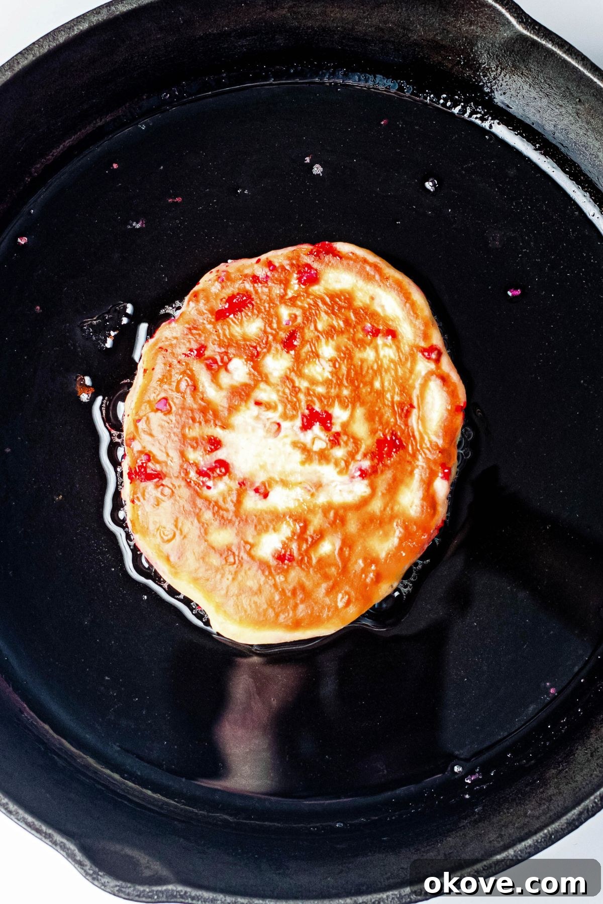 Sweetheart Pancakes 6 A perfectly golden-brown pancake, gently bubbling on a black nonstick skillet, indicating it's almost ready to be flipped and cooked to perfection.
