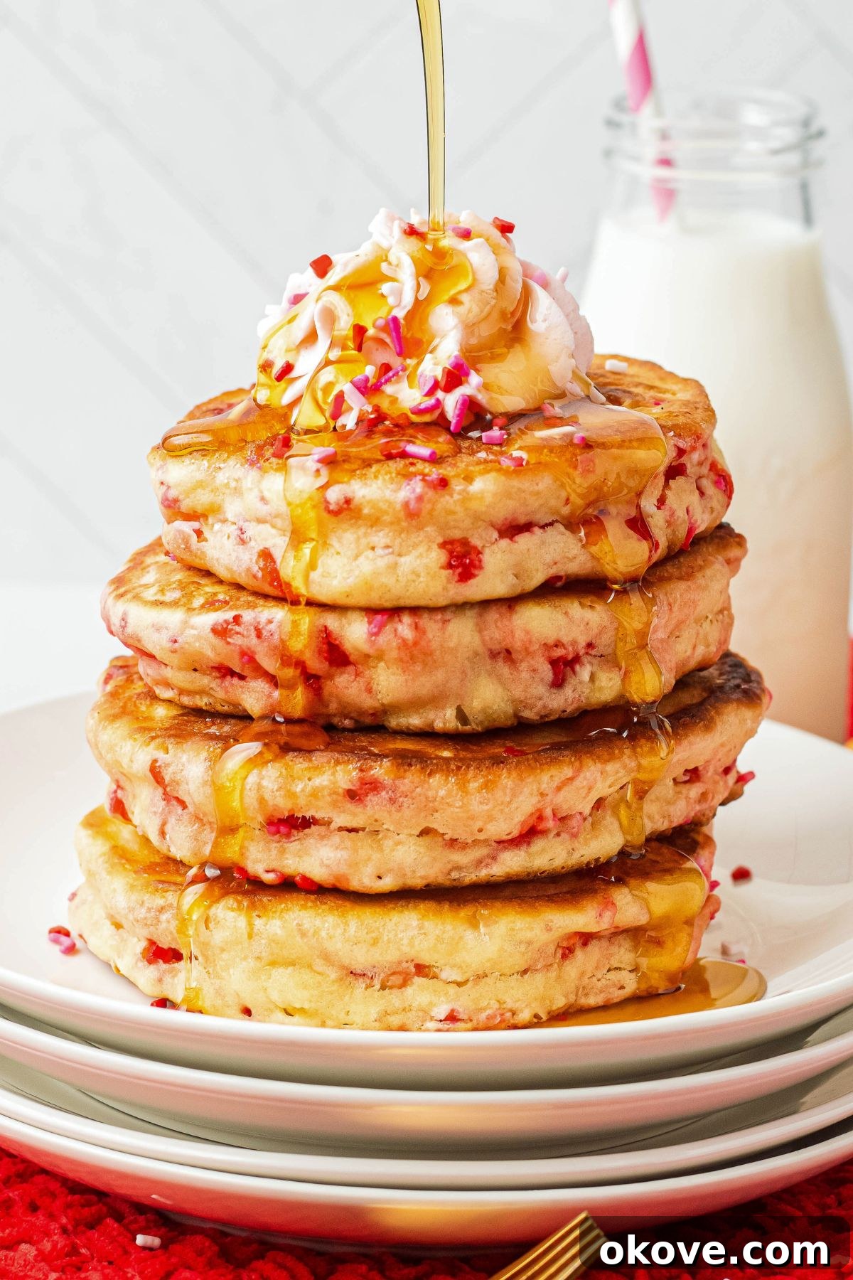 Sweetheart Pancakes 7 A tempting stack of golden, fluffy Valentine's Day pancakes on a white plate, with a generous cascade of rich maple syrup being poured gracefully over the top, making them even more irresistible.