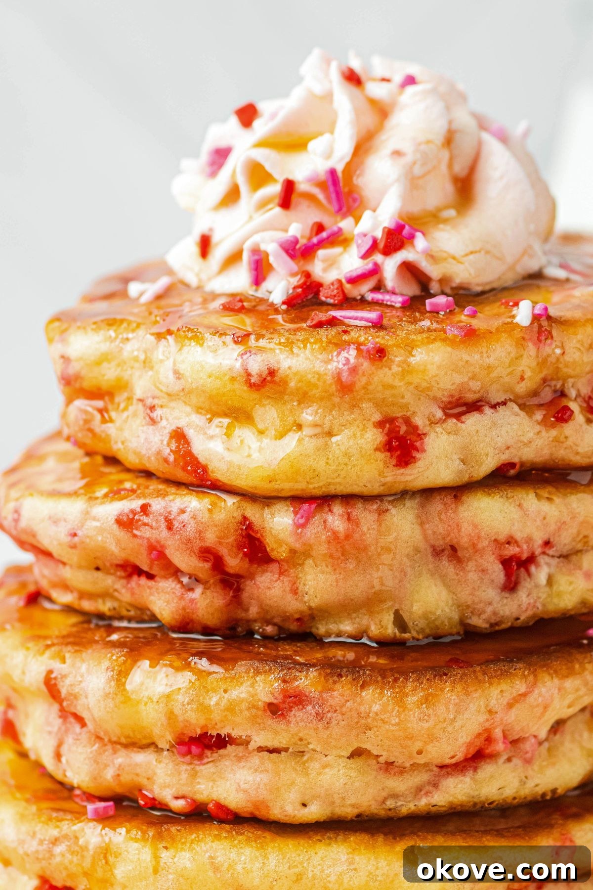Sweetheart Pancakes 8 A tempting close-up image of a stack of fluffy Valentine's Day pancakes, generously topped with a dollop of airy whipped cream and a festive scattering of colorful sprinkles, ready to be enjoyed.