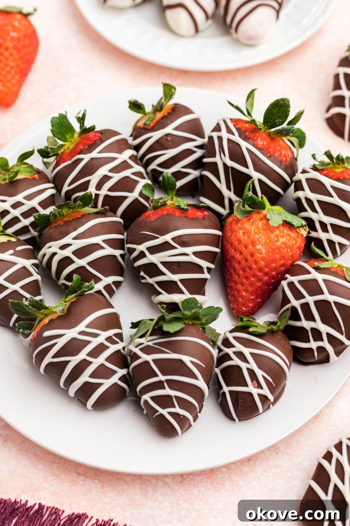 Effortless Chocolate Strawberry Delights 2 Chocolate covered strawberries on a white plate sitting on a pink table, ready to be enjoyed.