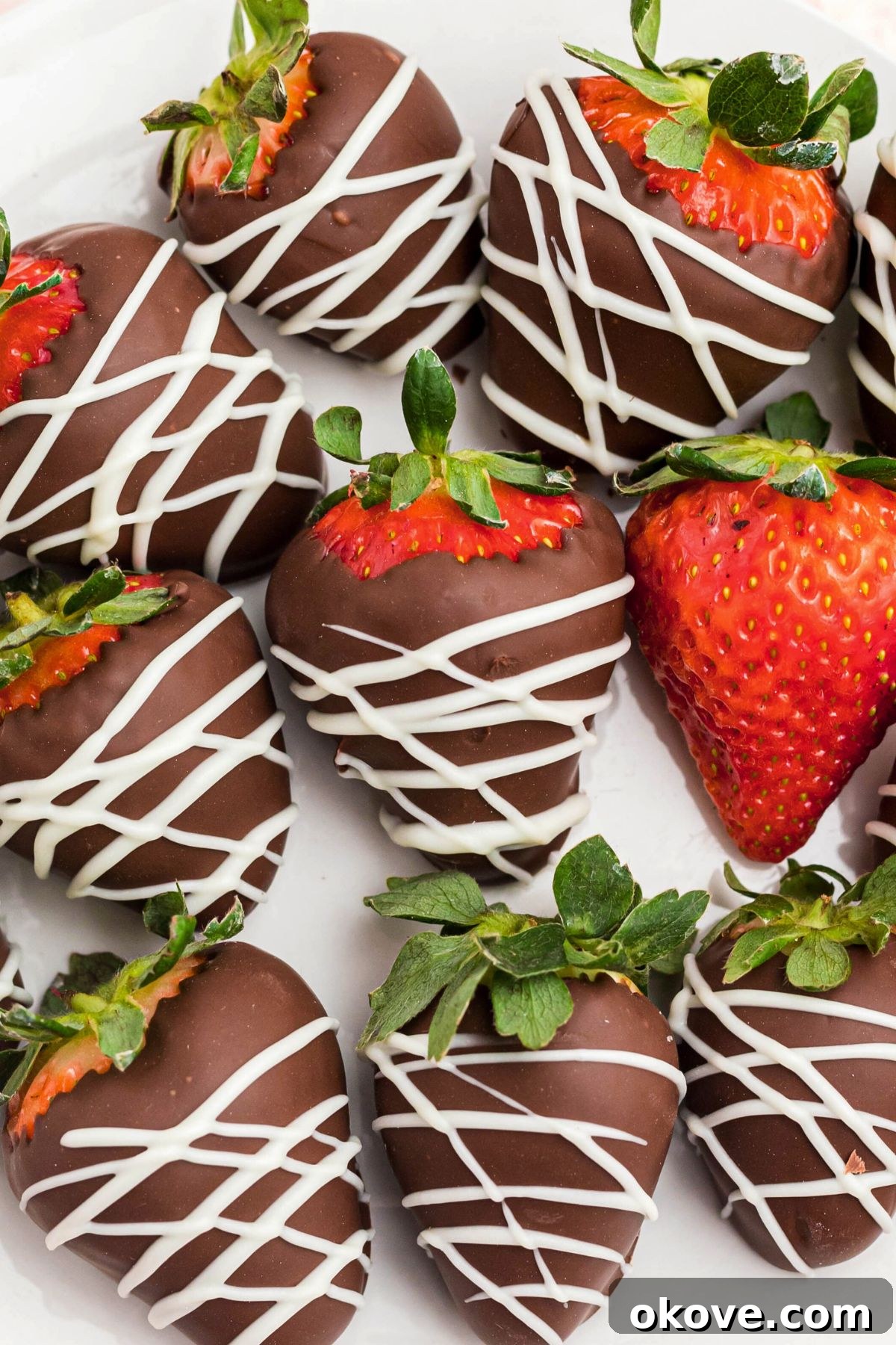 Effortless Chocolate Strawberry Delights 5 Strawberries coated with chocolate and white chocolate stripes, on a white plate with fresh strawberry in the center of plate.