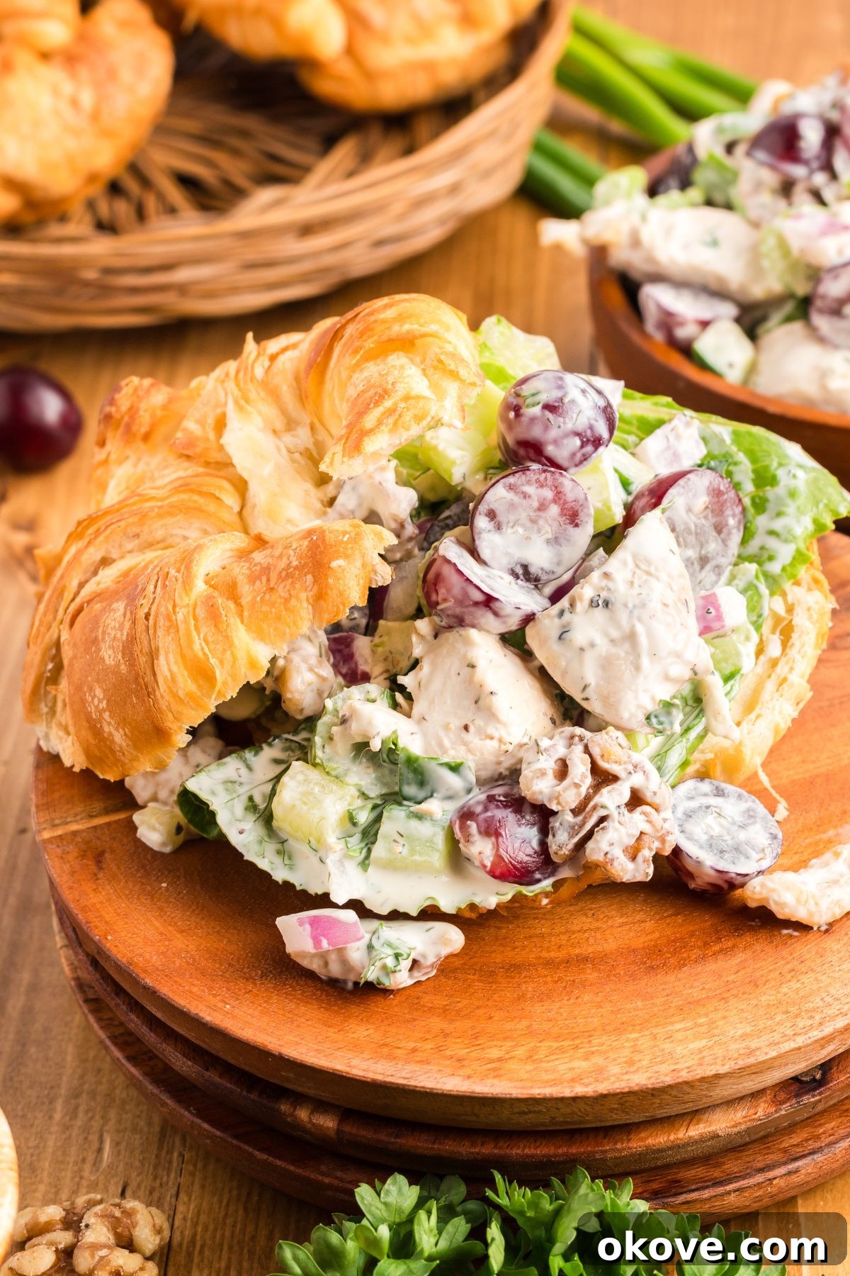 Orchard Chicken Salad 2 Creamy chicken salad with nuts and grapes, served elegantly in a croissant on a rustic wooden plate. The salad is a delightful mix of colors and textures, inviting a delicious bite.
