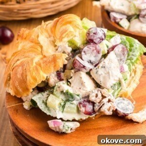 Creamy chicken salad with nuts and grapes, presented in a croissant on a wooden plate, ready for a delicious meal.