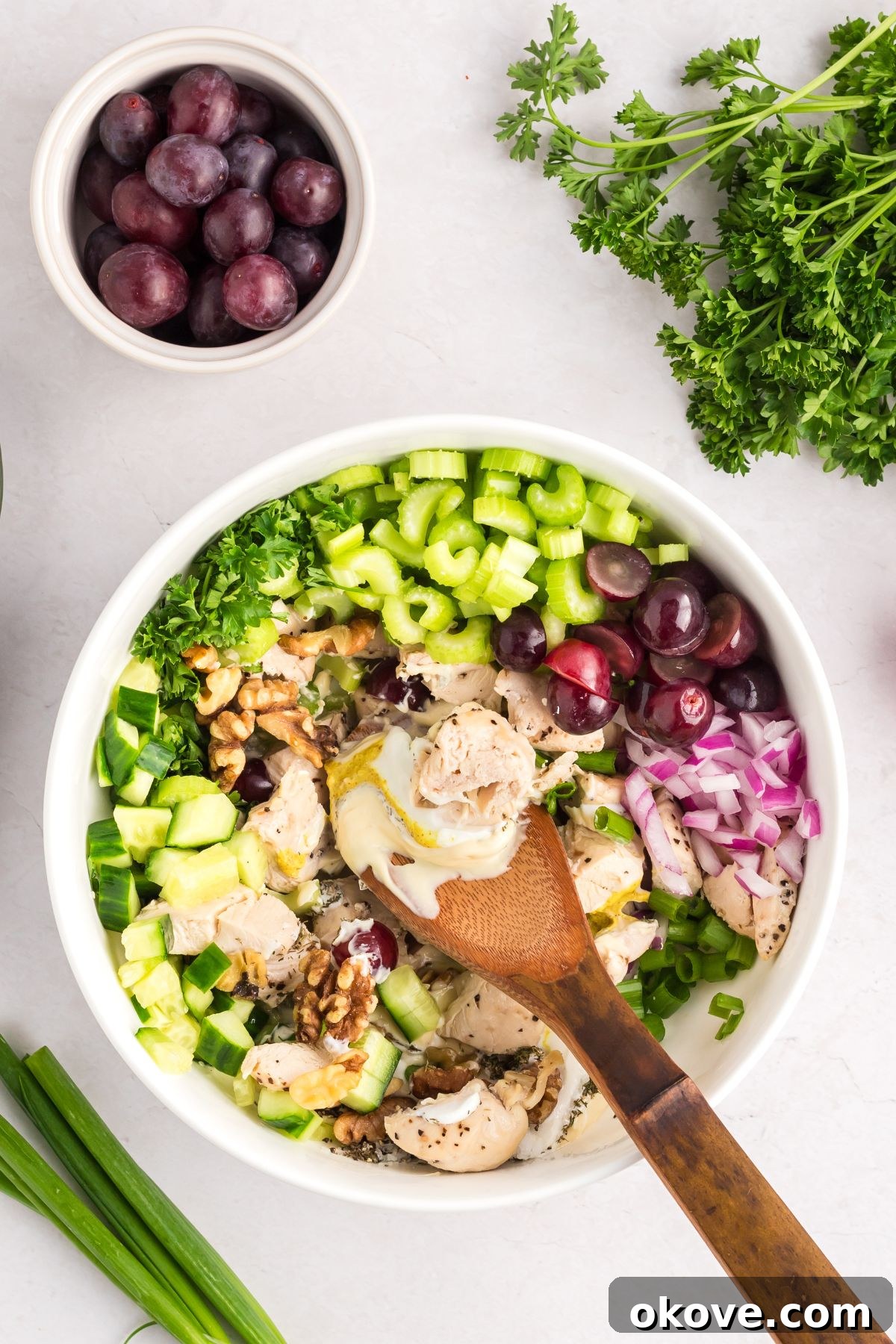 Orchard Chicken Salad 5 The creamy dressing ingredients, including mayonnaise, Greek yogurt, Dijon mustard, dried dill, salt, and pepper, are being whisked together in a separate small bowl with a wooden spoon until smooth and well combined.