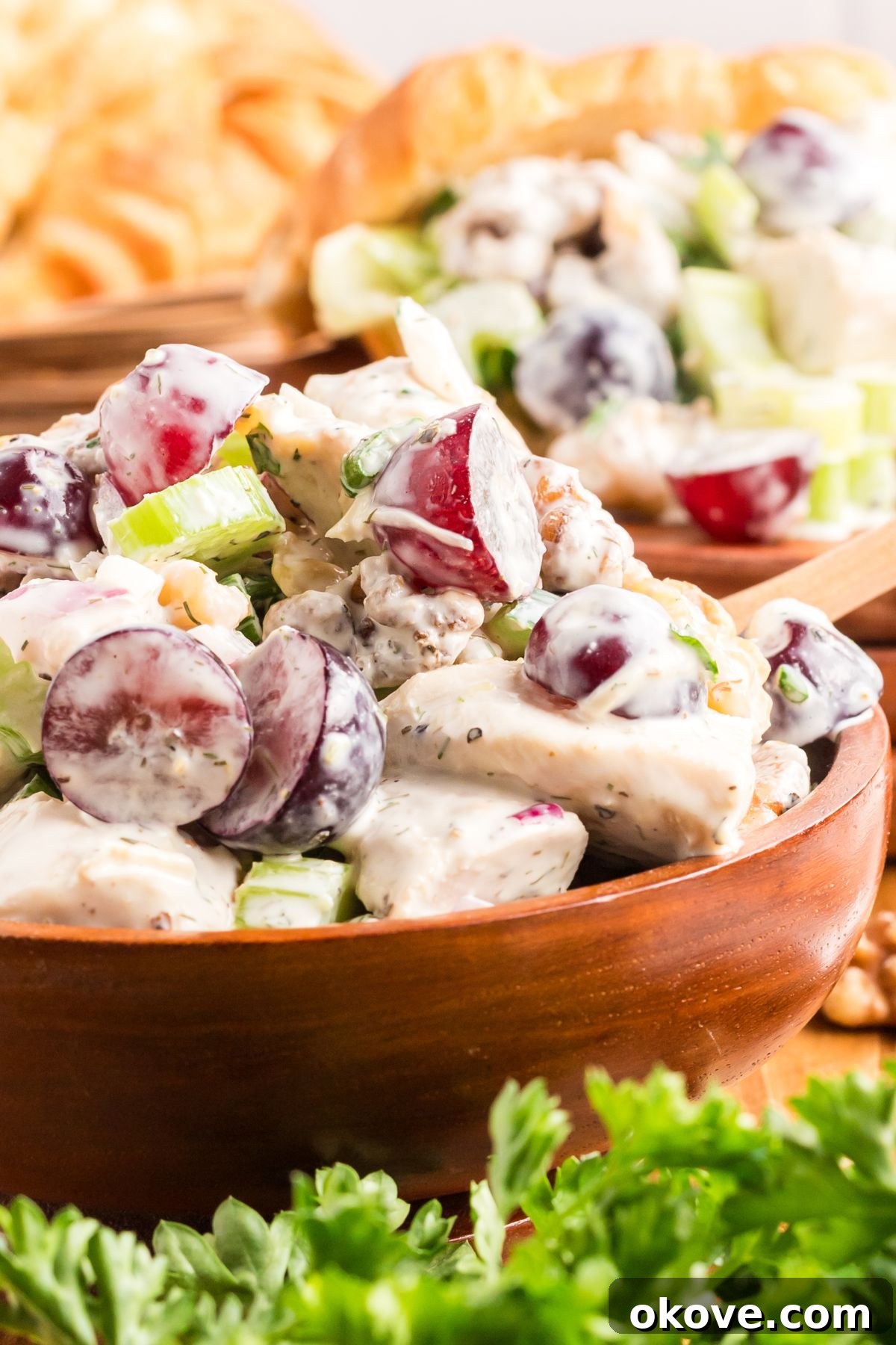 Orchard Chicken Salad 7 A vibrant and creamy chicken salad with grapes, beautifully presented in a stylish wooden bowl, accompanied by fresh green garnishes in the foreground, ready for serving.