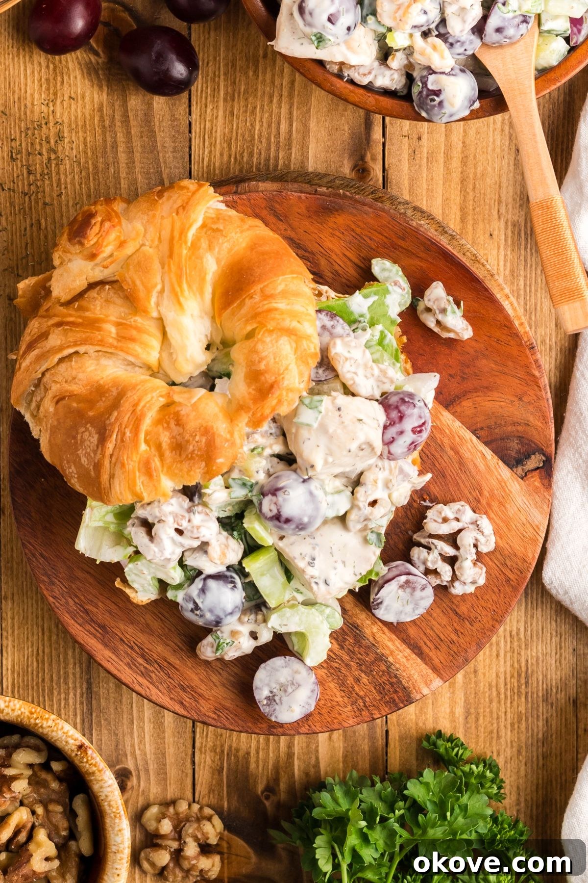 Orchard Chicken Salad 8 An inviting overhead shot of a classic chicken salad sandwich, beautifully assembled in a flaky croissant and served on a warm wooden plate, ready to be savored.