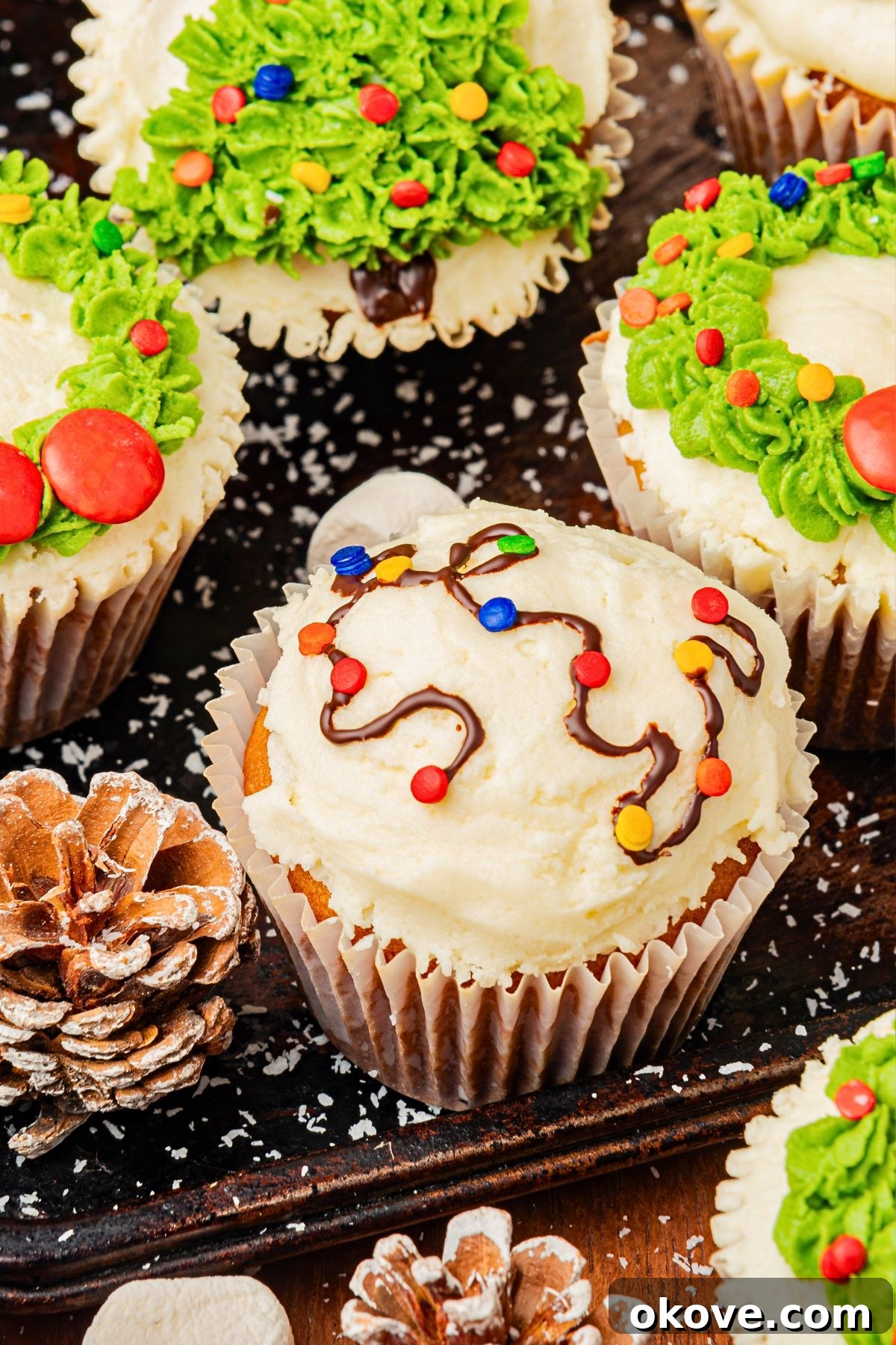 Merry & Bright Christmas Cupcakes 11 A festive array of Christmas cupcakes adorned with various holiday decorations, including snowmen, wreaths, and string lights, presented beautifully on a table.