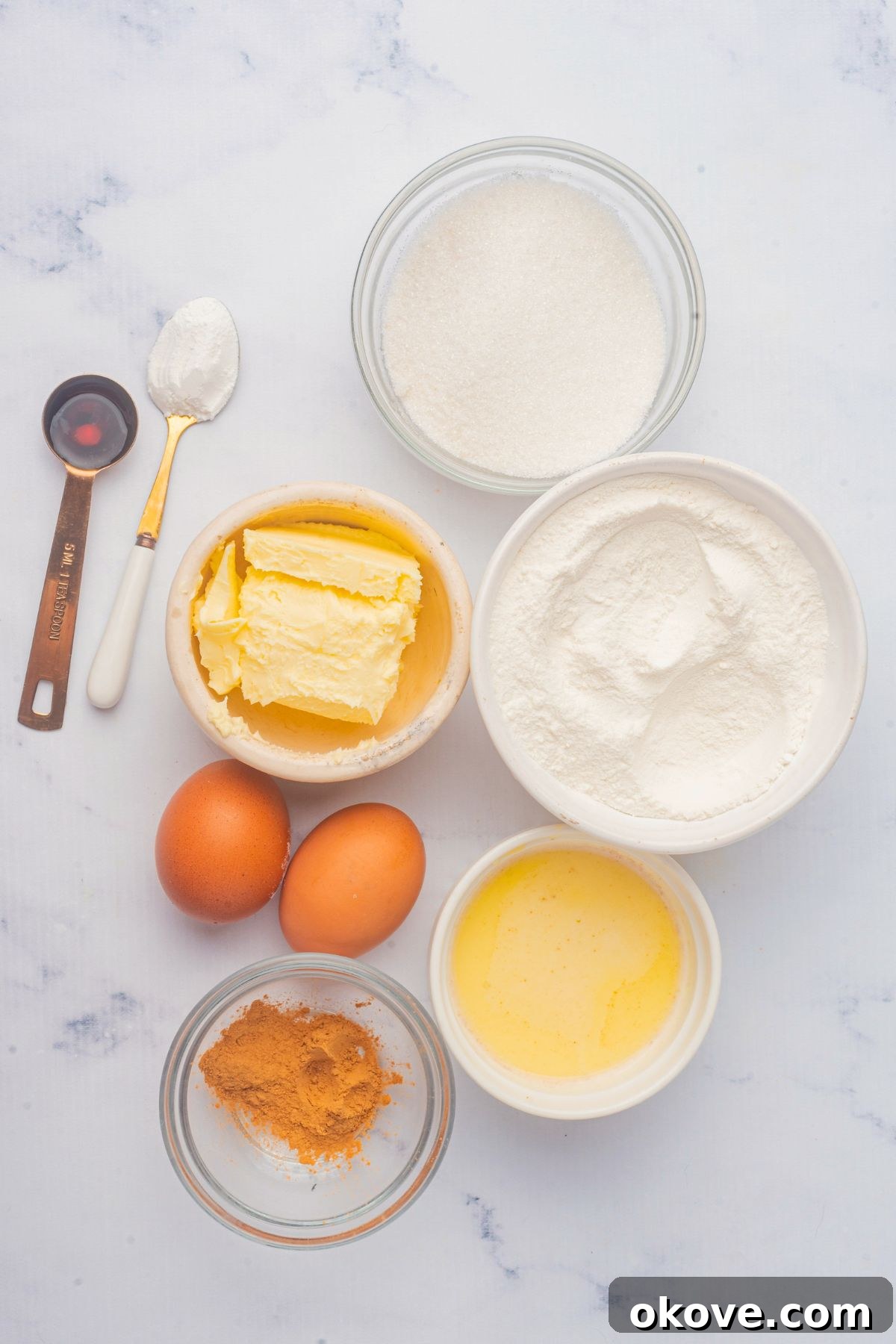Merry & Bright Christmas Cupcakes 3 Precisely measured cupcake ingredients including flour, sugar, butter, and eggnog, neatly arranged in small glass bowls on a white marble countertop.