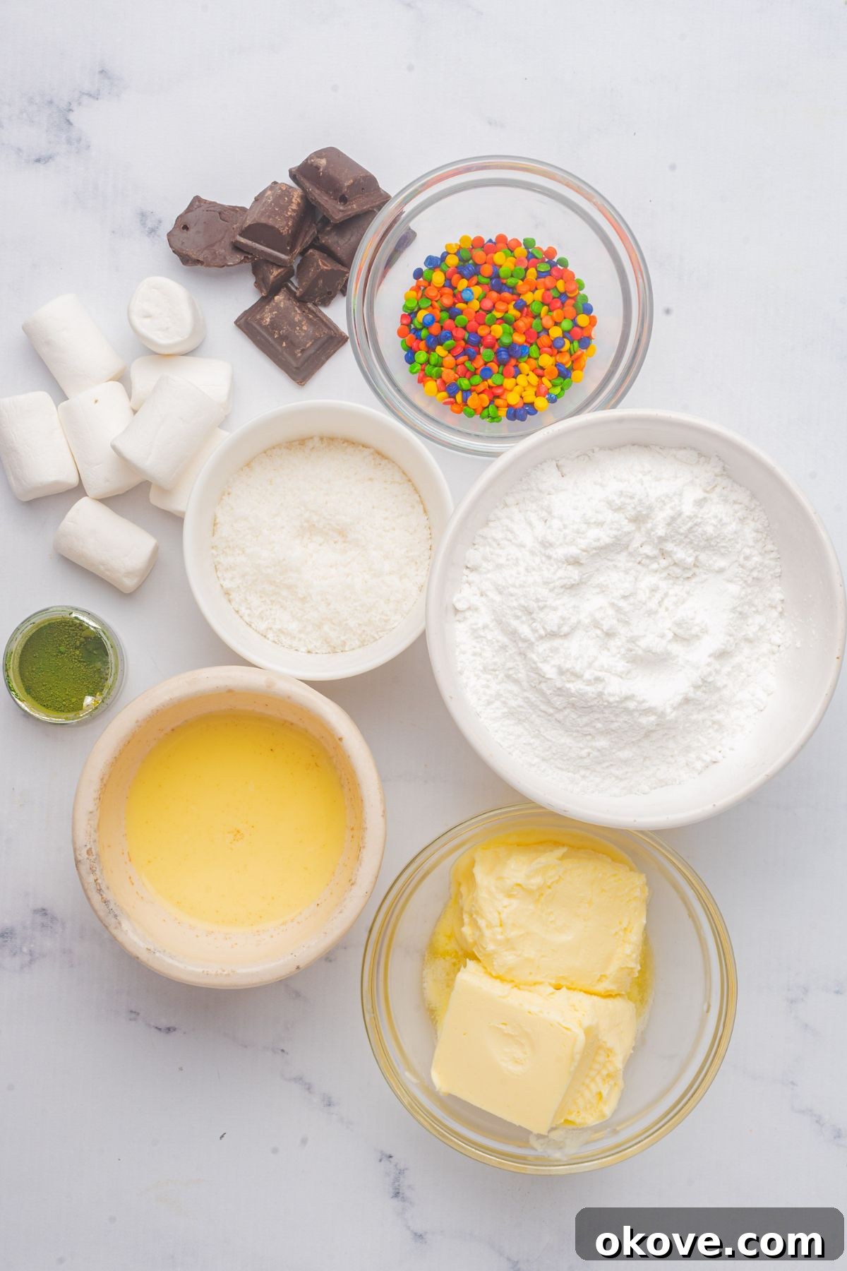 Merry & Bright Christmas Cupcakes 4 Eggnog buttercream frosting ingredients and various cupcake decorations like sprinkles, marshmallows, and dark chocolate, meticulously arranged in small glass bowls on a pristine white marble table.