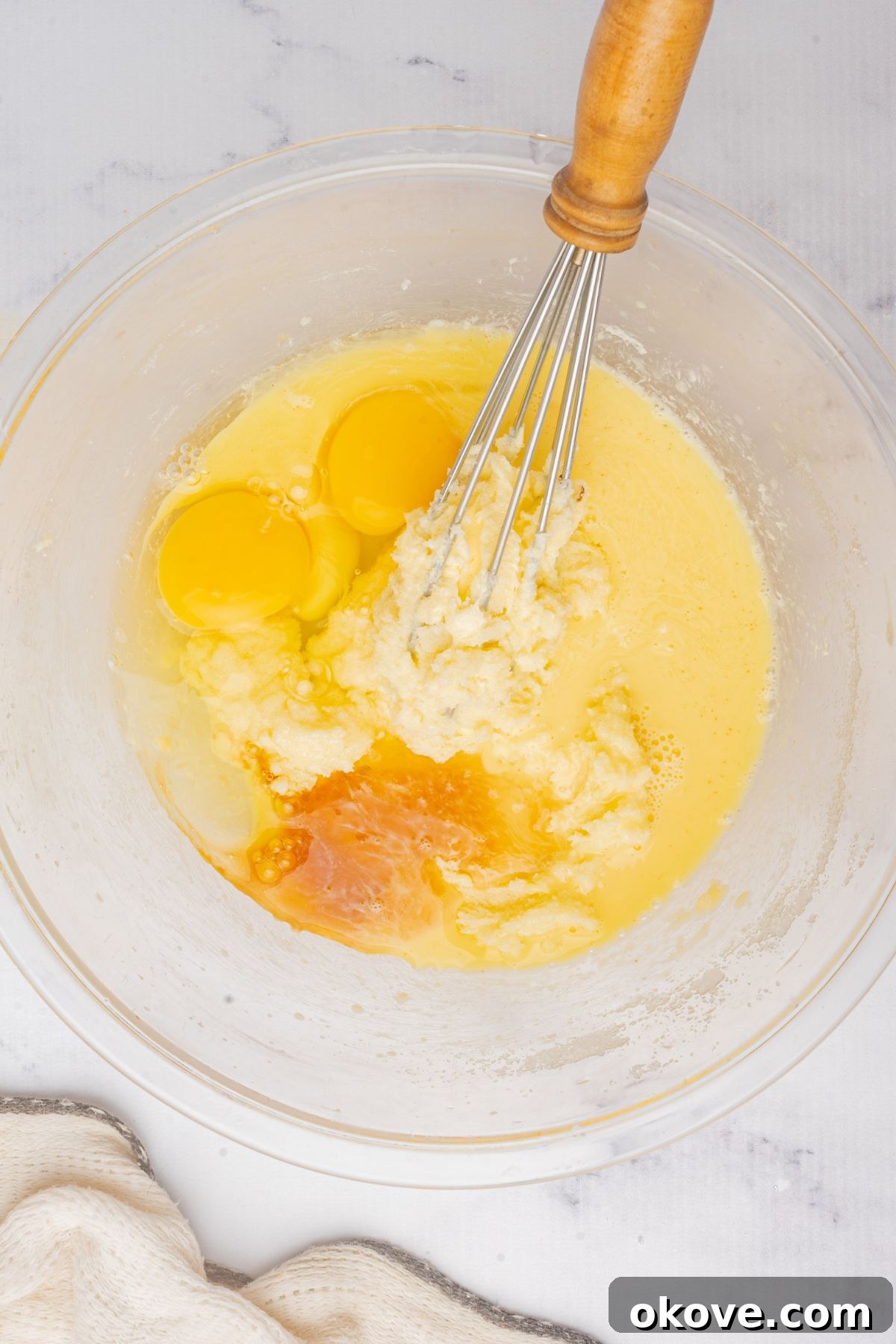 Merry & Bright Christmas Cupcakes 5 Softened butter and granulated sugar being creamed together in a large clear glass mixing bowl with an electric hand mixer, creating a light and fluffy mixture.