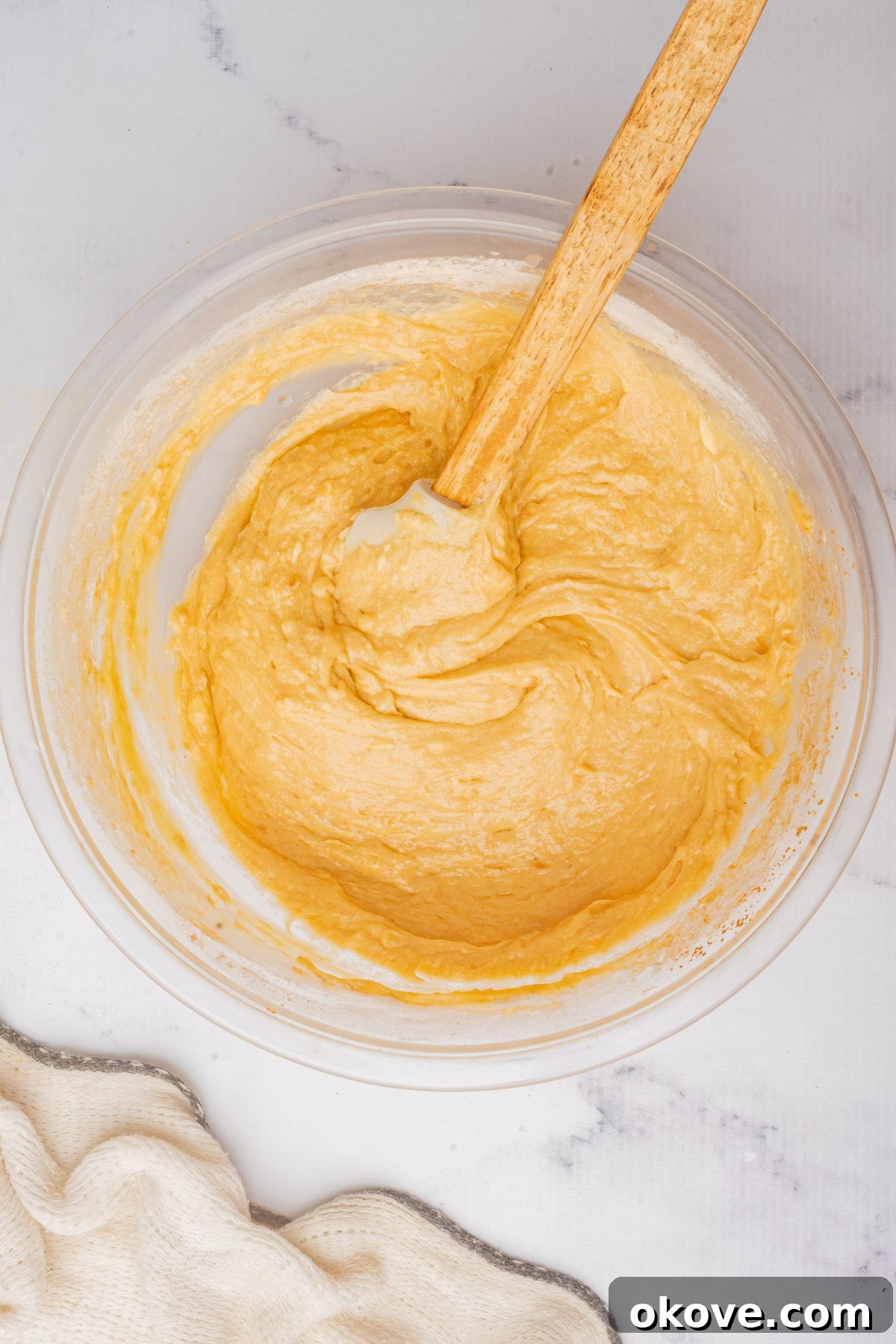 Merry & Bright Christmas Cupcakes 6 Smooth, well-combined cupcake batter in a large glass bowl, stirred gently with a wooden spoon, ready to be portioned into cupcake liners.