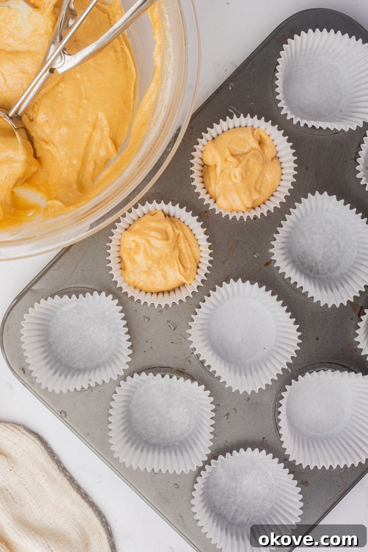 Merry & Bright Christmas Cupcakes 7 Cupcake liners being precisely filled with light yellow cake batter using a portion scoop, ensuring even distribution for uniform baking results.