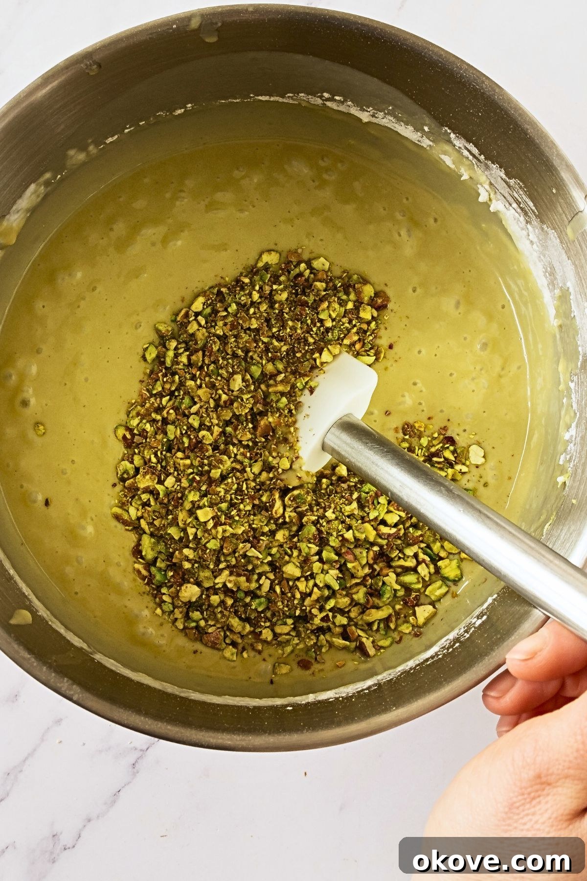 Emerald Pistachio Bundt 5 Chopped pistachios being folded into cake mix in a silver bowl.