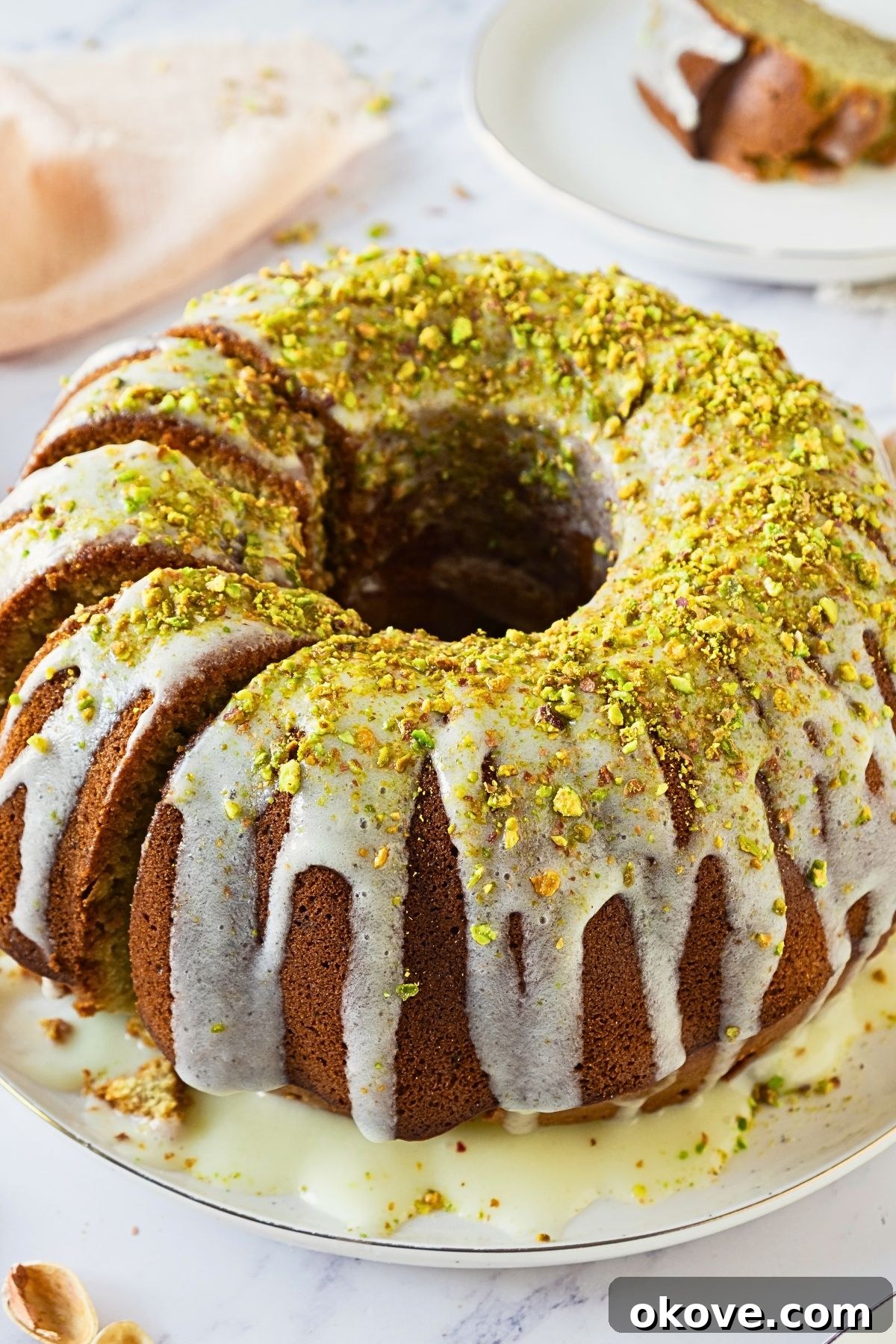 Emerald Pistachio Bundt 8 Bundt cake on a platter with a few slices made into the left side of the cake.