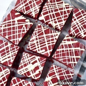 Bright red brownies cut into squares with white chocolate drizzled on top.