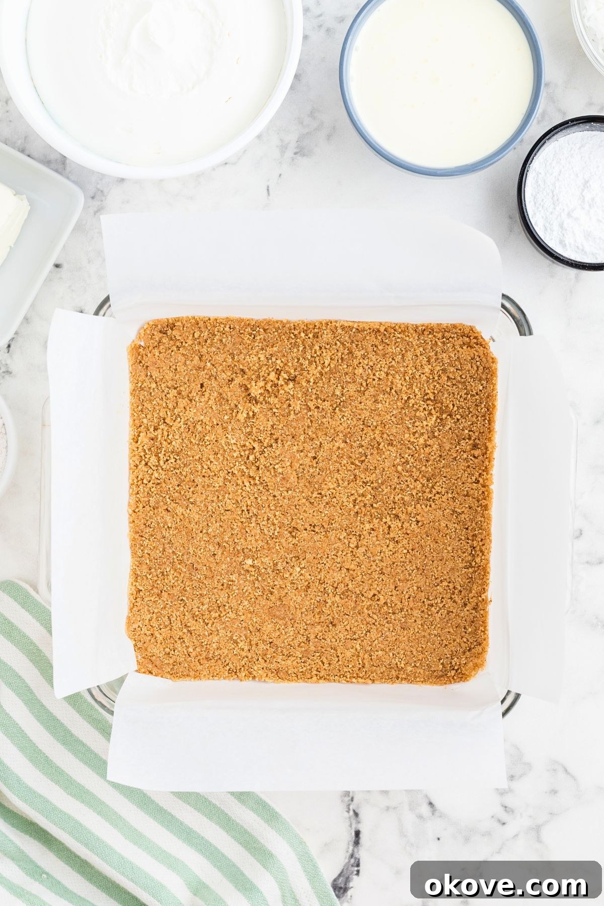 Paradise Coconut Indulgence 5 The graham cracker crust mixture, combined with melted butter, has been pressed firmly and evenly into the bottom of a baking dish, forming a solid base for the dessert.