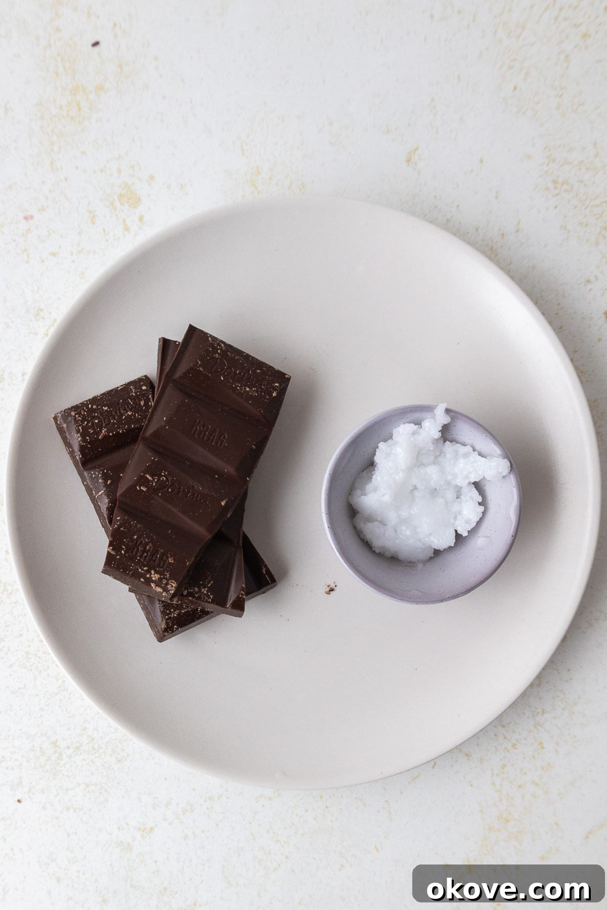 The Secret to Perfect Chocolate Curls 3 Chocolate and coconut oil on a small white plate before being combined to make chocolate curls.