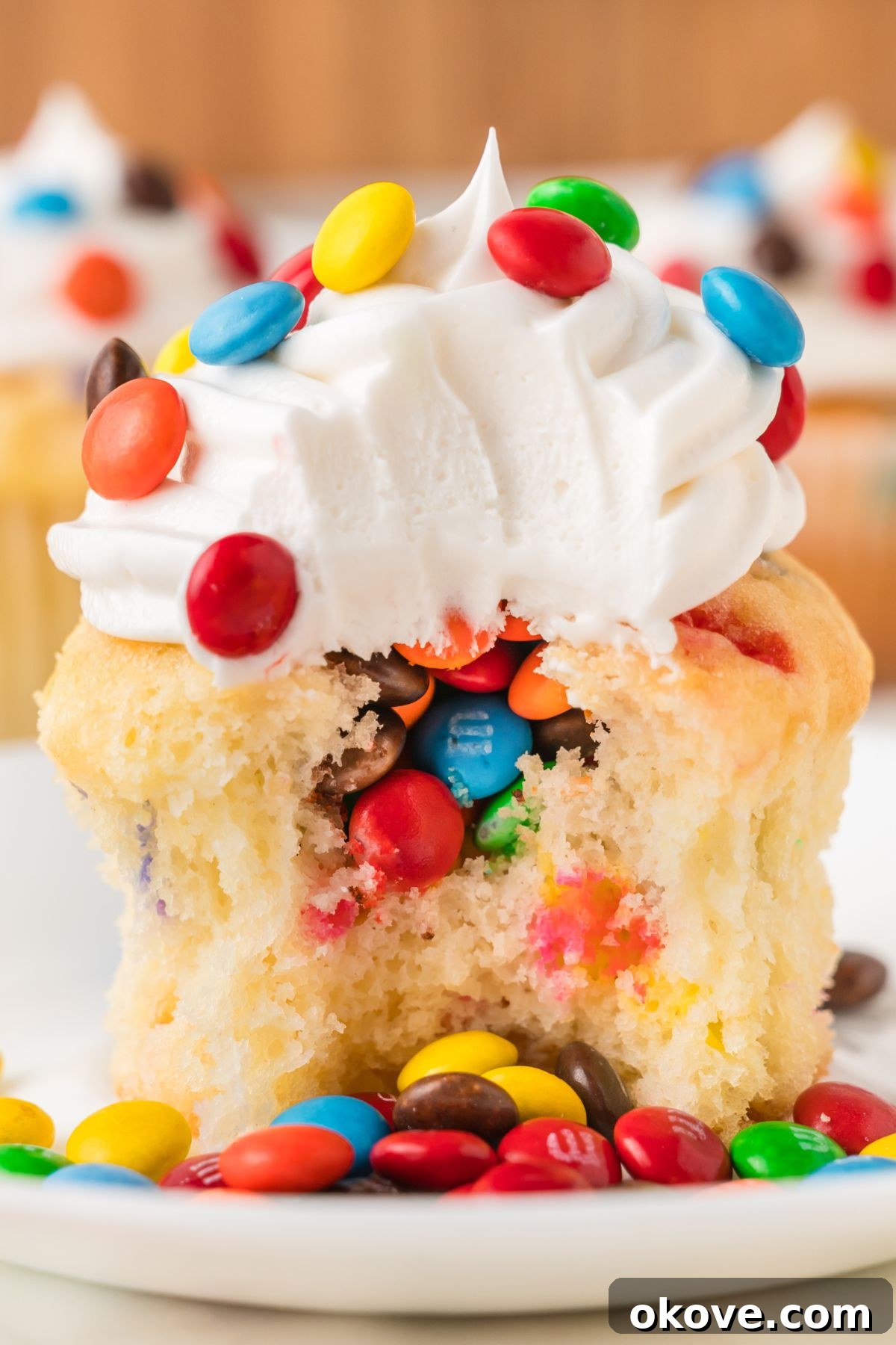 A beautifully decorated M&M cupcake with vanilla frosting and colorful candies on top.