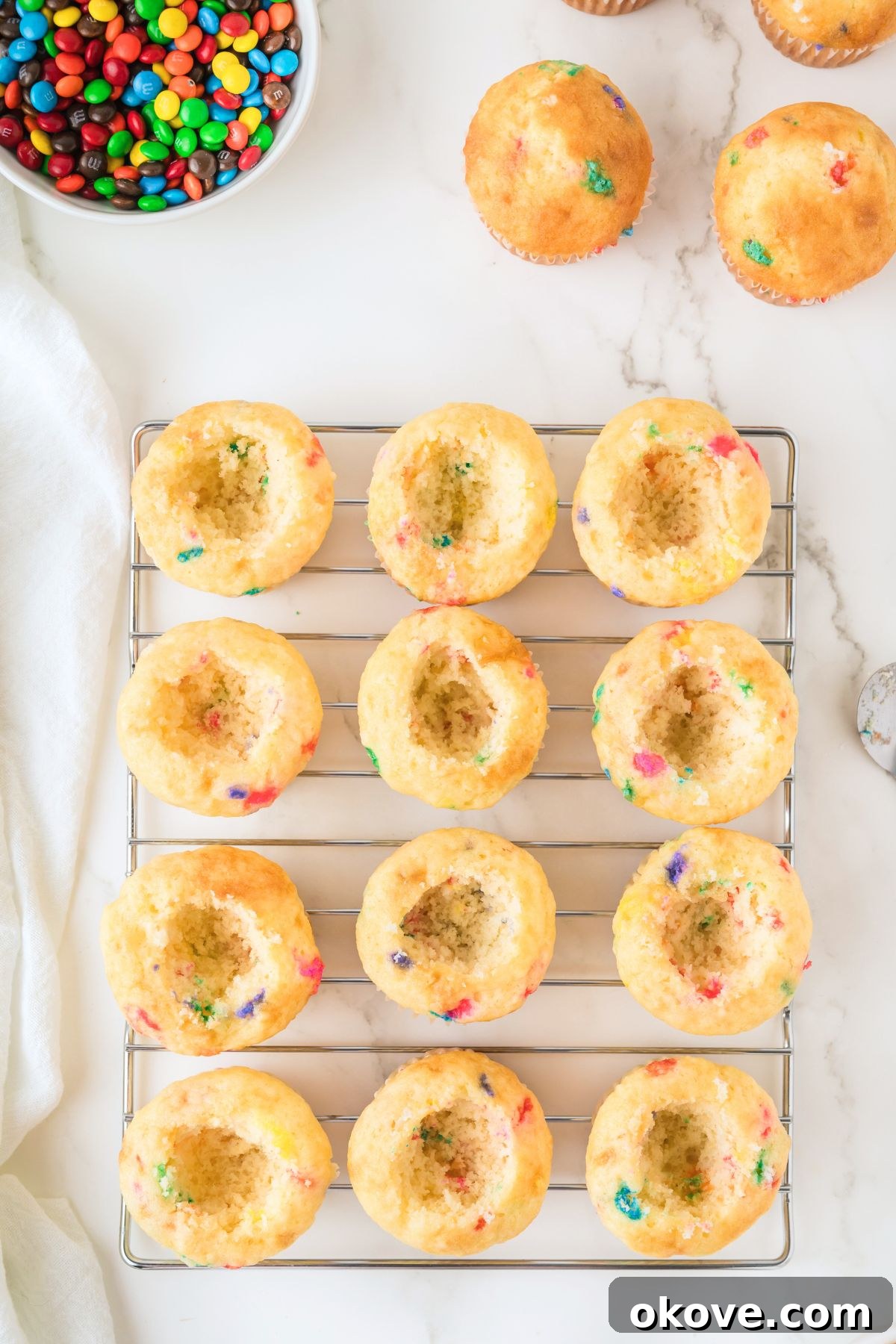 Freshly baked funfetti cupcakes cooling on a wire rack, with a small scoop removed from the center of each, ready for filling.