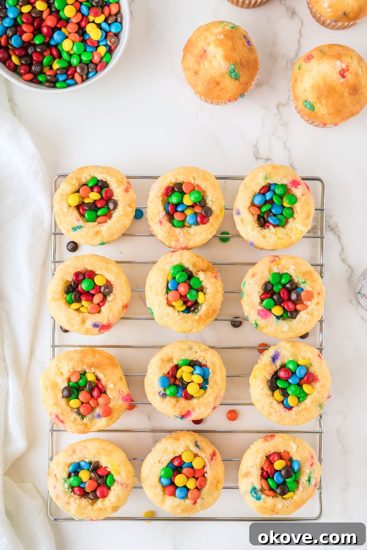 Vanilla cupcakes with centers scooped out and generously filled with colorful mini M&Ms, waiting to be frosted.