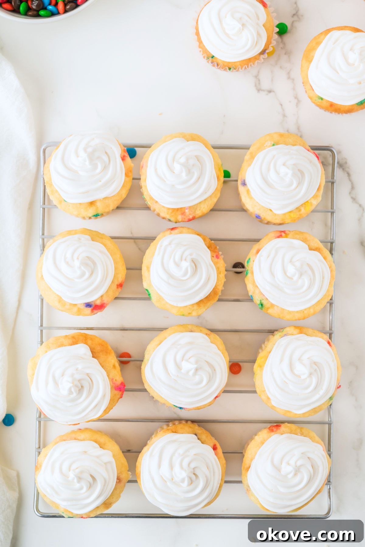Beautifully frosted cupcakes with creamy vanilla frosting, arranged on a cooling rack, ready for the final touch of M&Ms.